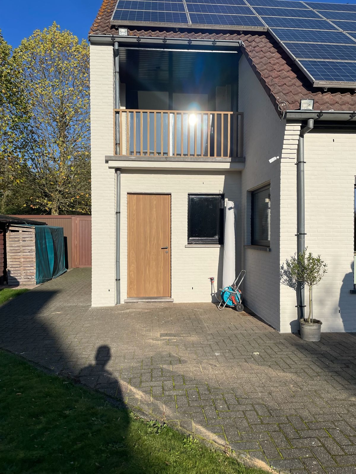 Achtergevel met houten buitendeur en houten balkonbalustrade op de verdieping in Zevergem.