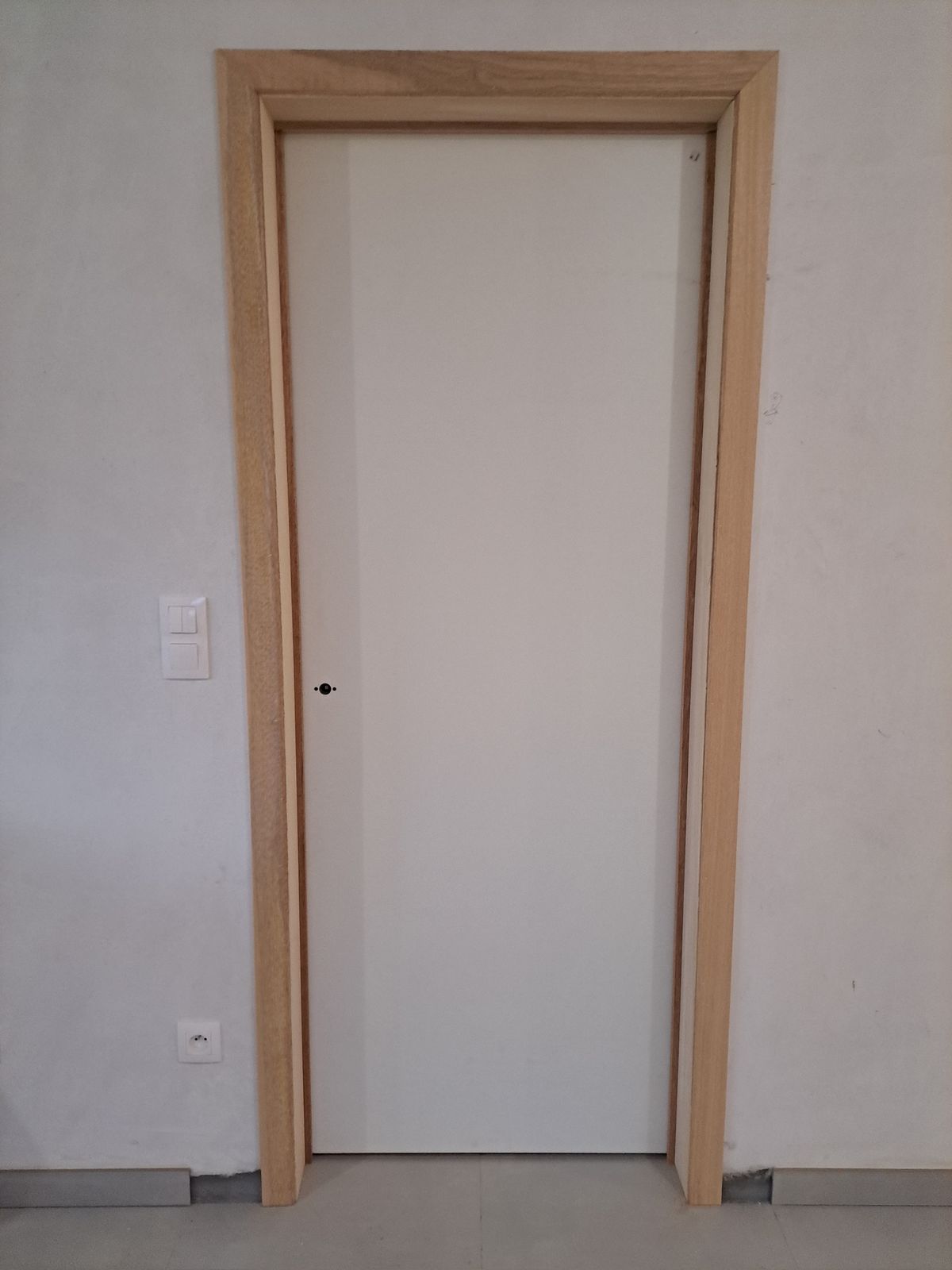 Witte binnendeur met brede houten deuromlijsting tegen een gepleisterde muur in Hamme.