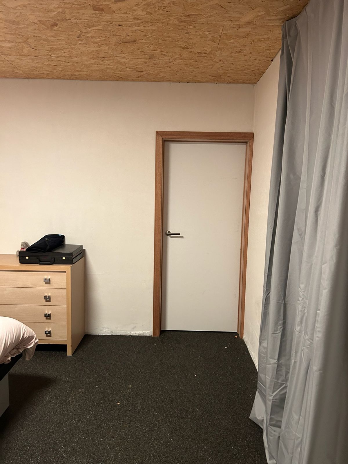 Witte binnendeur met houten deurkader in een slaapkamer met donkere vloer in Lendelede.