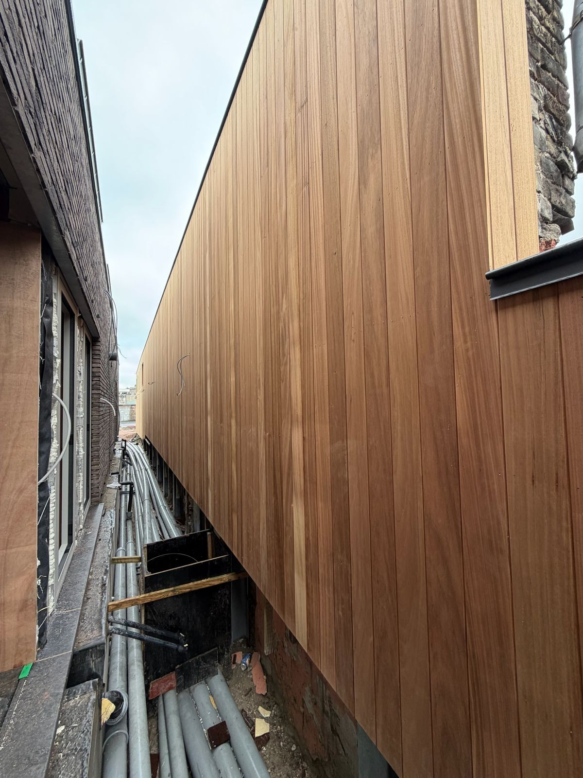 Cederhouten gevelbekleding op de bovenverdieping van een nieuwbouw gezien vanuit de zijgang in Sint-Kruis.