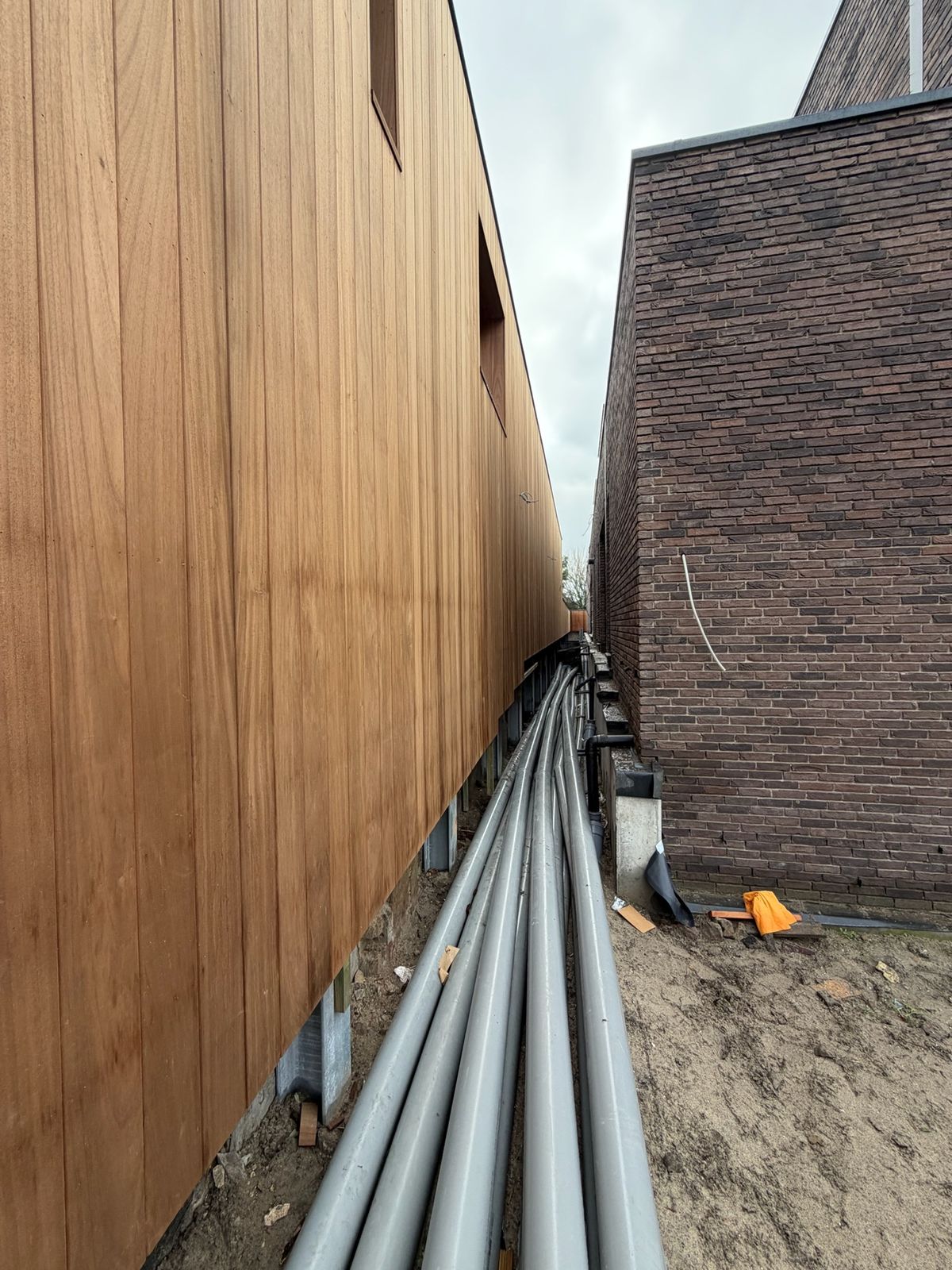 Verticale cederhouten gevelbekleding langs een smalle zijgevel naast bakstenen buren in Sint-Kruis.