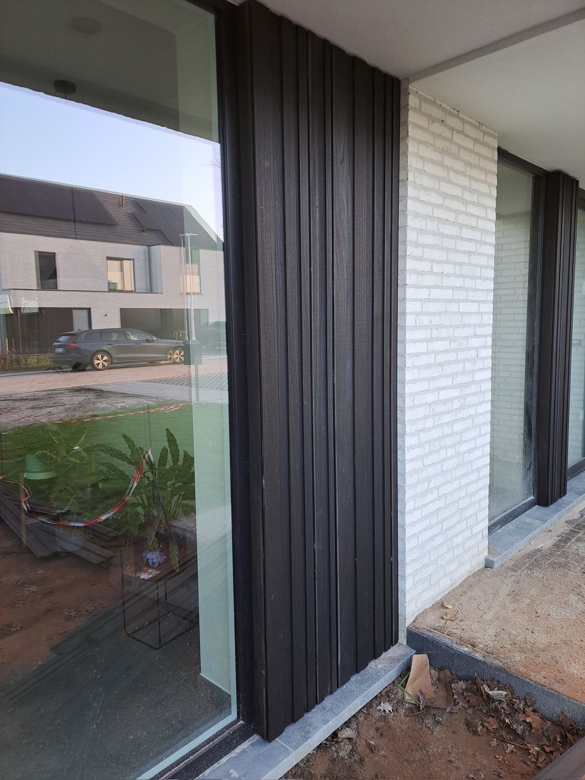 Donkere houten gevelplanken naast een groot raam en witte baksteen in Lokeren.