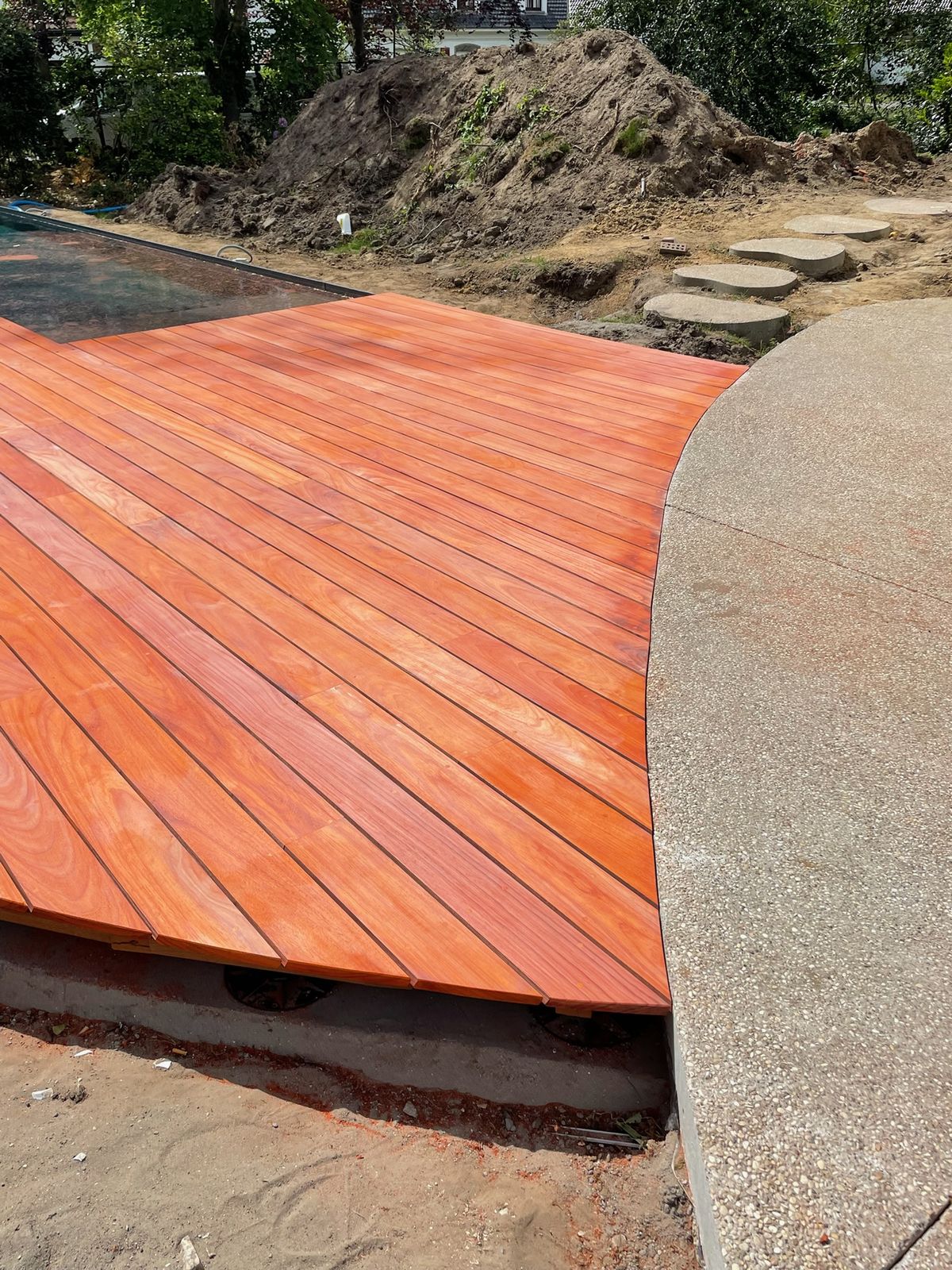 Hardhouten terras met gebogen rand naast een betonpad aan het zwembad in De Pinte.