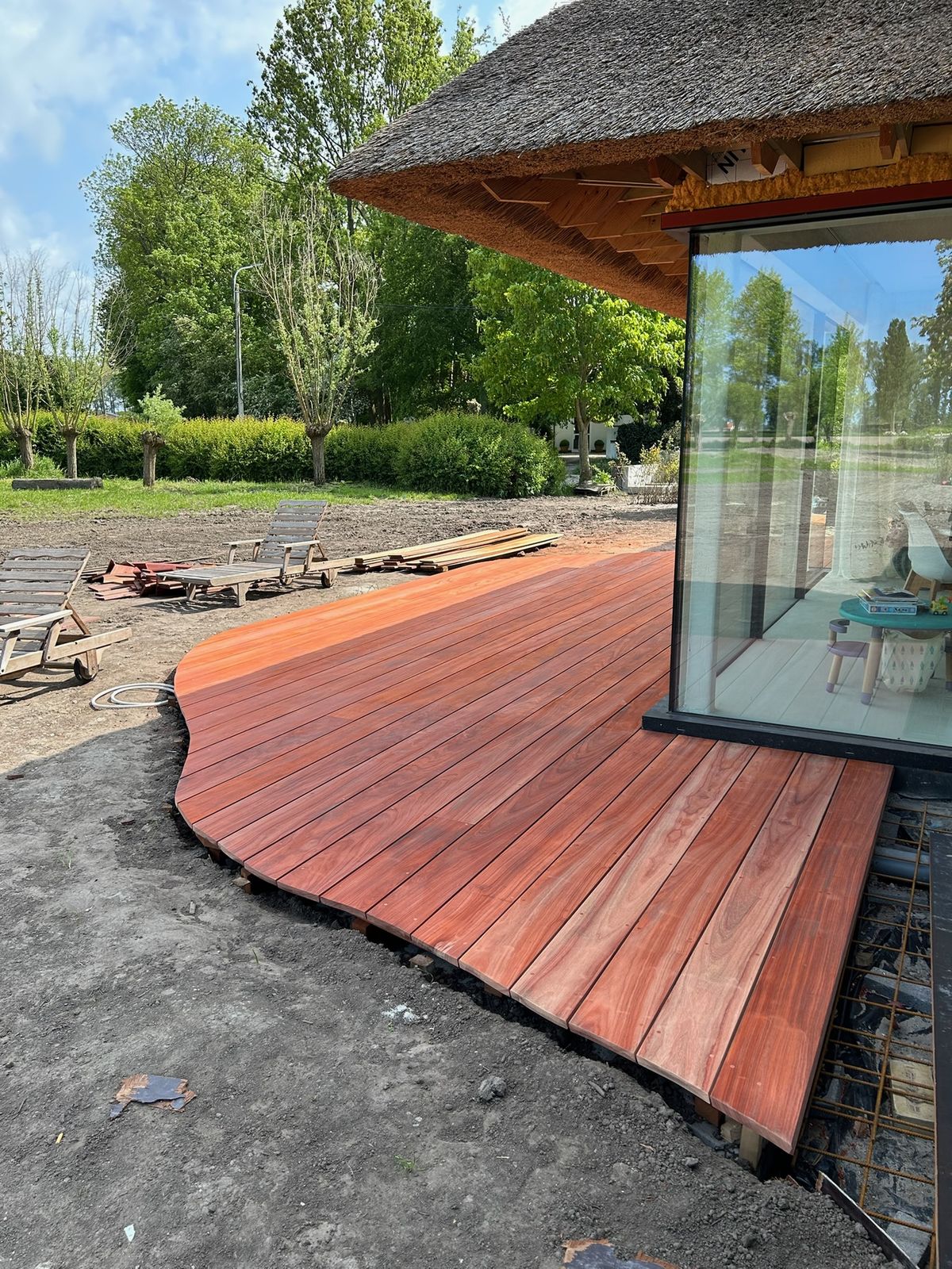 Gebogen hardhouten terras rond de hoek van een woning met rieten dak in Oostkerke.
