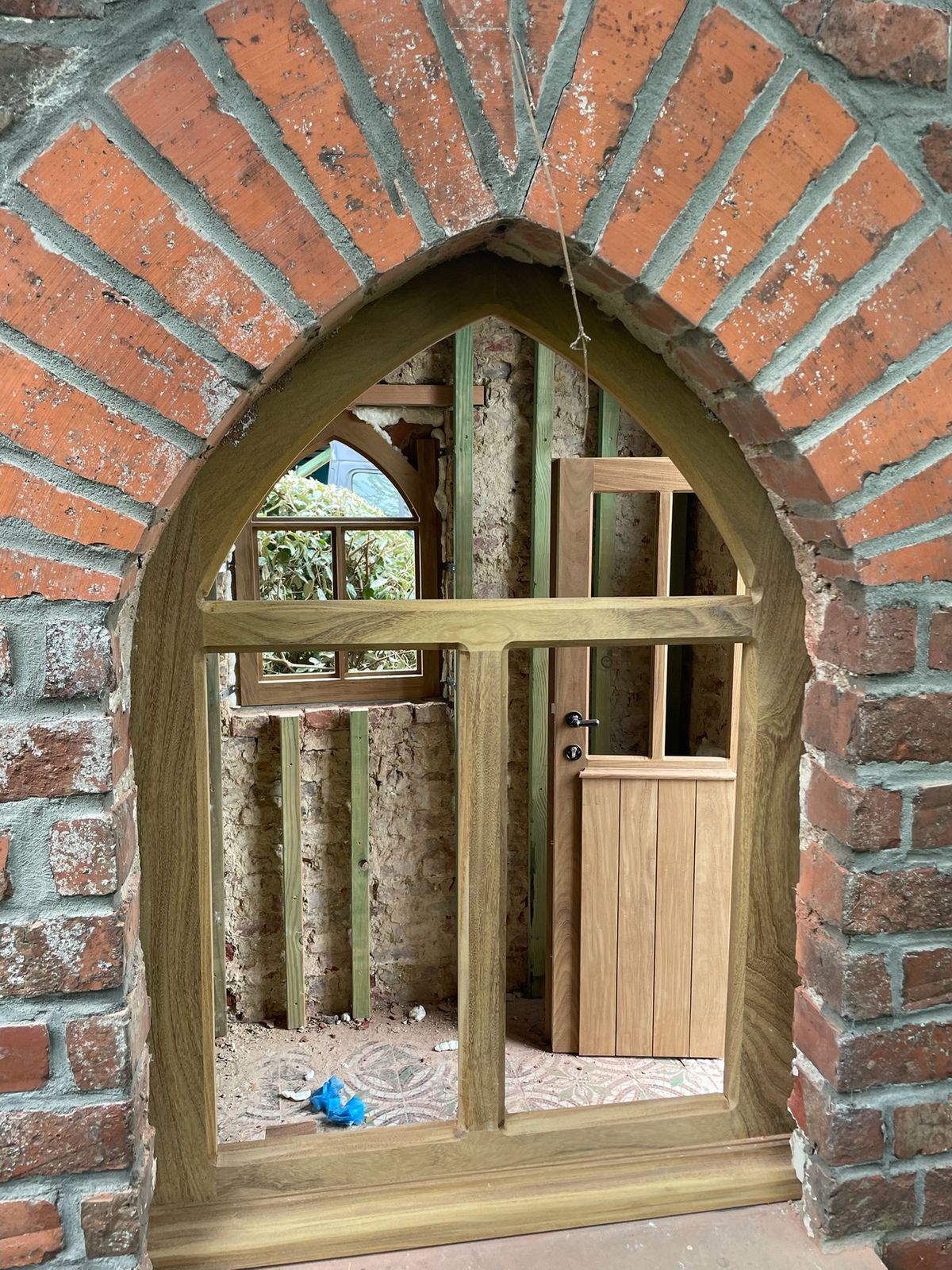 Gotische houten deur met spitsboog en bovenlicht in een bakstenen muuropening in Waregem.