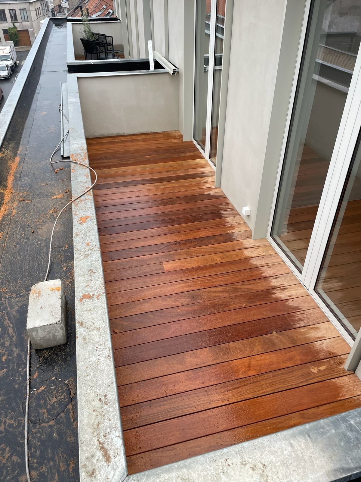 Nieuwe hardhouten balkonvloer langs de schuiframen van een appartement in Gent.