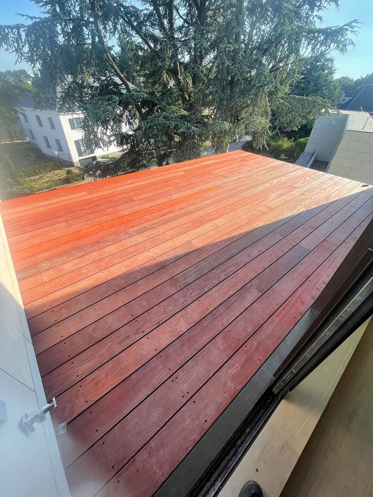 Hardhouten dakterras met roodbruine planken en zicht op het groen in Gent.