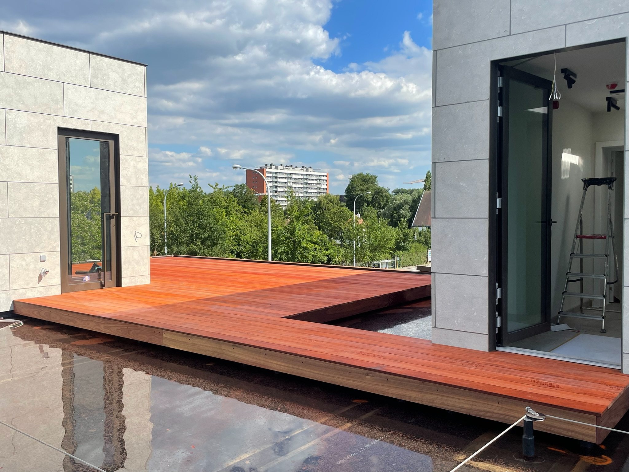 Hardhouten dakterras op maat aan een appartement met glazen schuifdeur