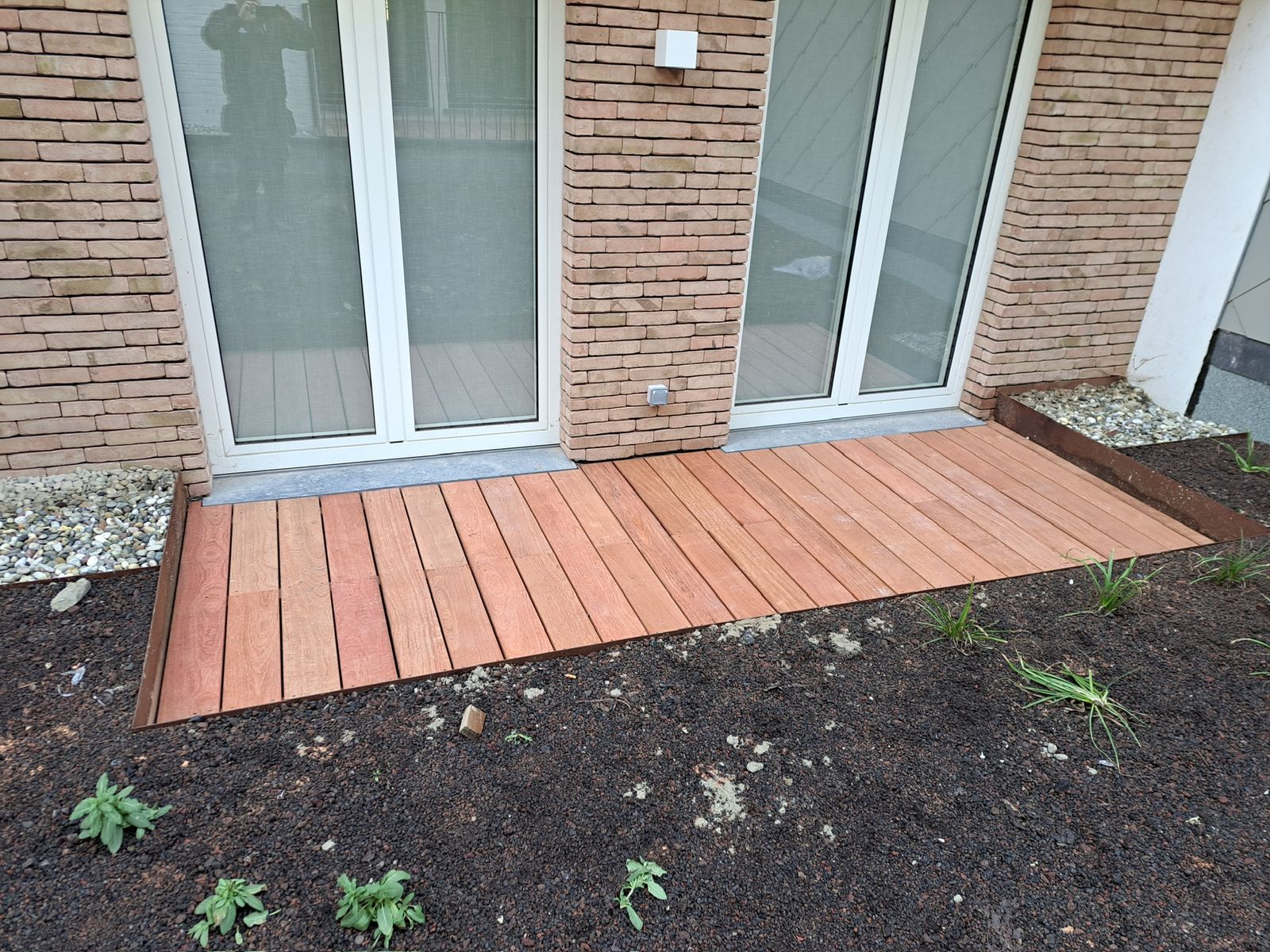 Hardhouten terras langs de achtergevel voor twee raampartijen van een woning in Gent.