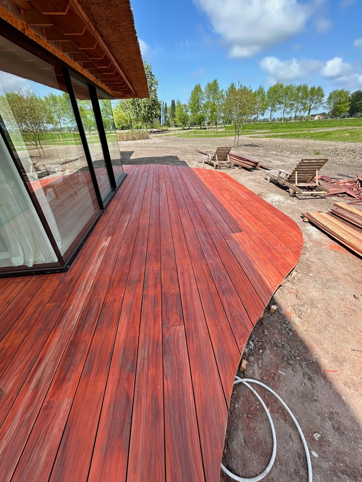 Lang hardhouten terras met golvende rand langs de glazen gevel van een villa in Oostkerke.