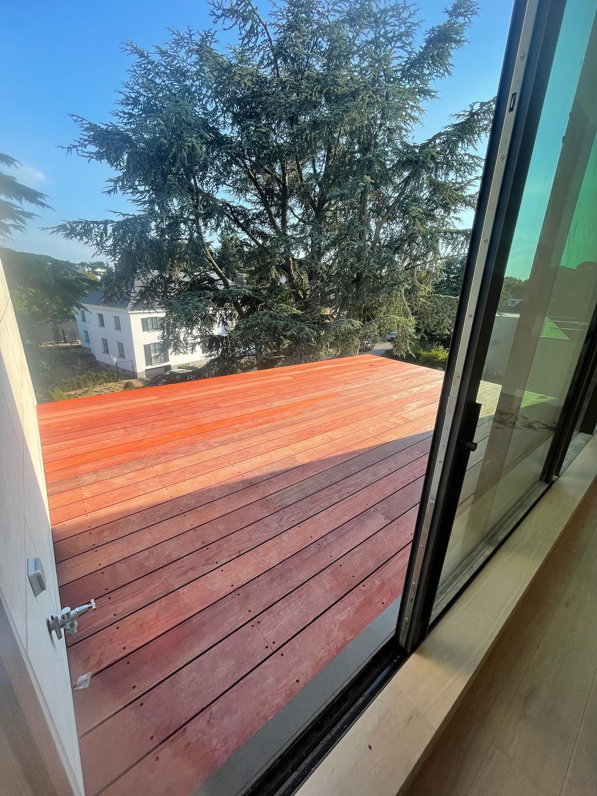 Hardhouten terras gezien vanuit een open schuifraam met bomen op de achtergrond in Gent.