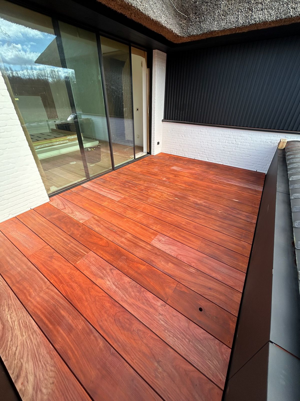 Rood hardhouten terras voor grote schuiframen van een moderne woning in Knokke-Heist.