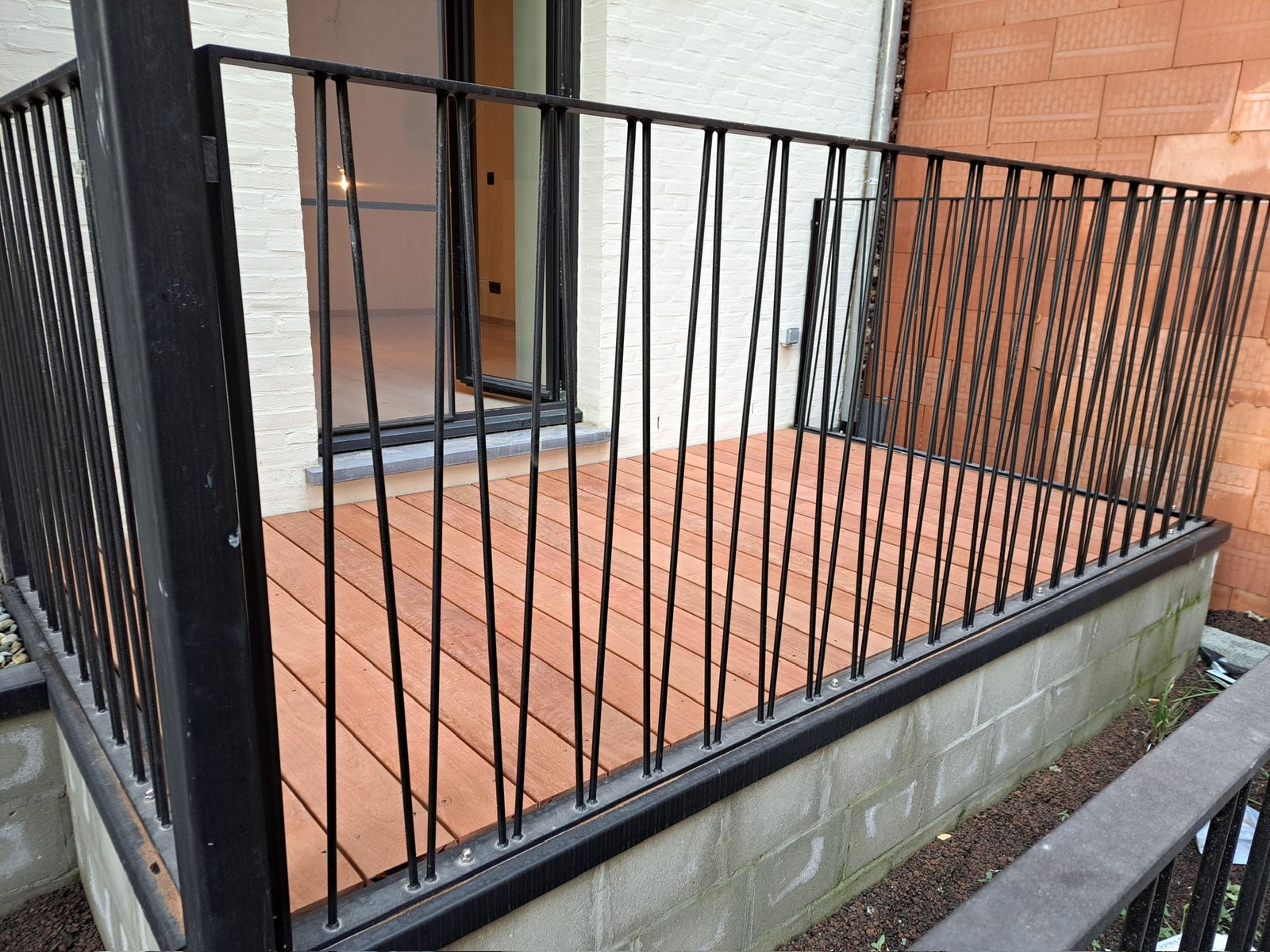 Hardhouten terras met zwarte metalen balustrade aan de achtergevel van een woning in Gent.