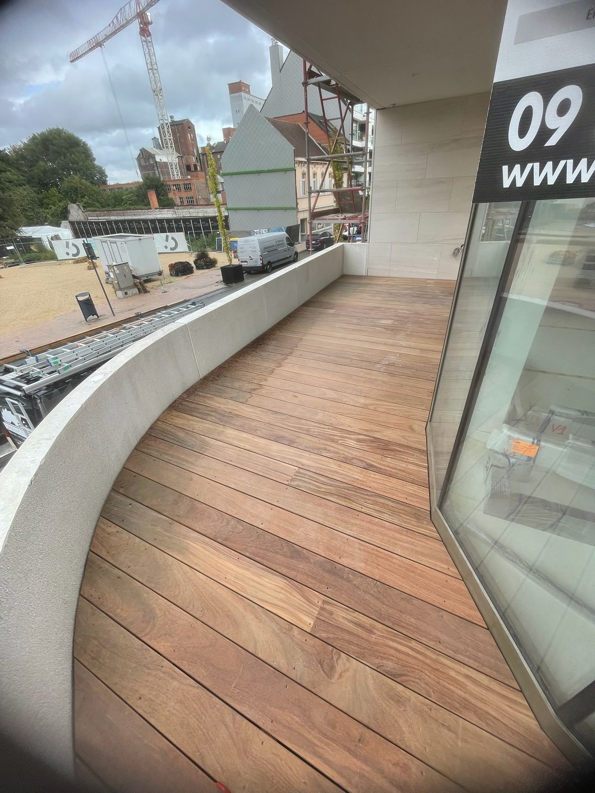 Hardhouten terrasplanken volgen de ronde betonnen borstwering van een balkon in Deinze.