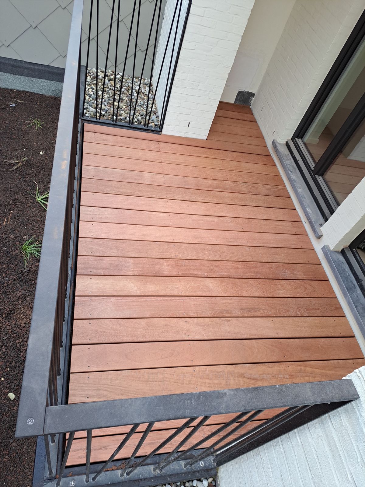 Hardhouten terrasplanken voor een schuifraam met zwarte balustrade in een tuin in Gent.