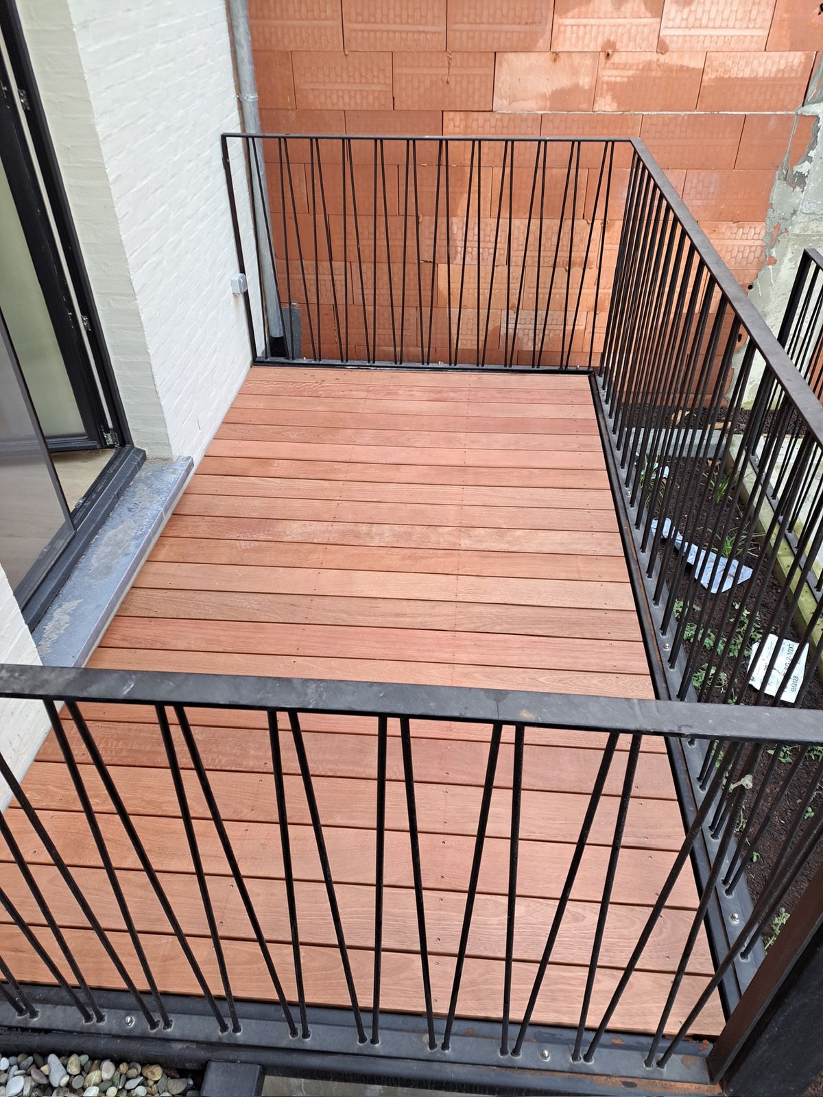 Bovenaanzicht van een hardhouten terrasvloer omringd door een zwarte balustrade in Gent.