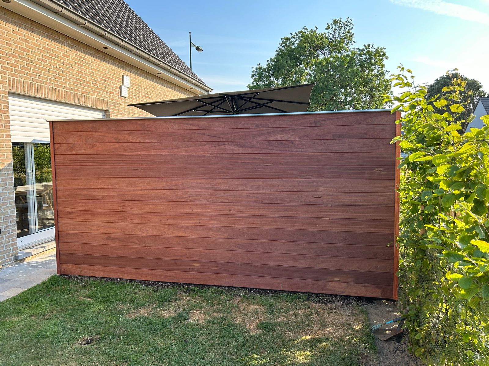 Hardhouten tuinscherm met horizontale planken op het gazon naast de woning in Lotenhulle.