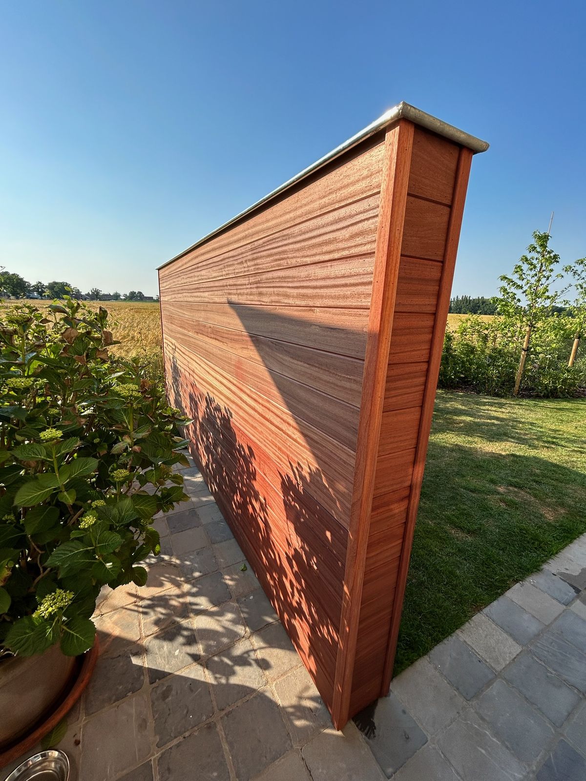 Hardhouten tuinscherm met horizontale planken naast een terras in Lotenhulle.