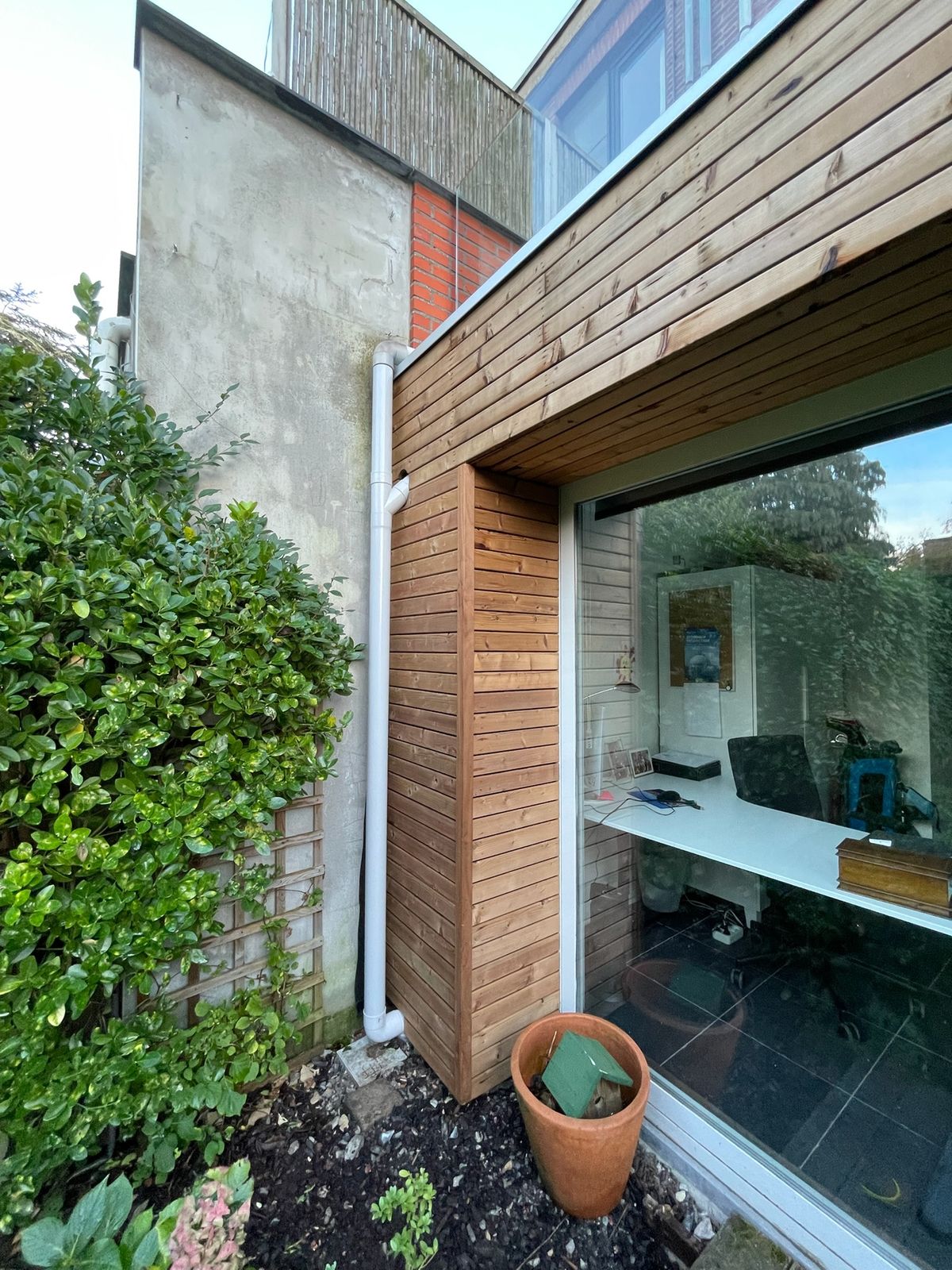 Horizontale houten gevelbekleding rond een groot raam aan de tuinzijde van een woning.
