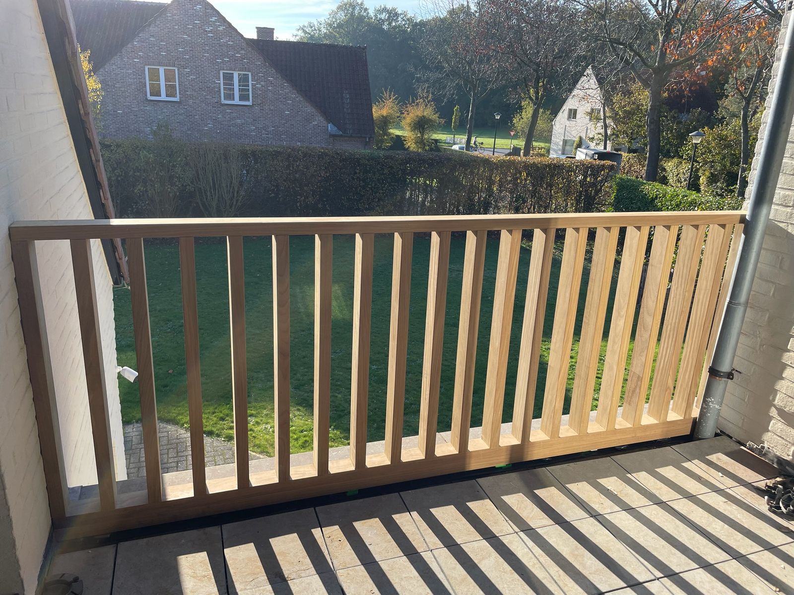 Houten balustrade met verticale spijlen op een balkon met zicht op de tuin in Zevergem.
