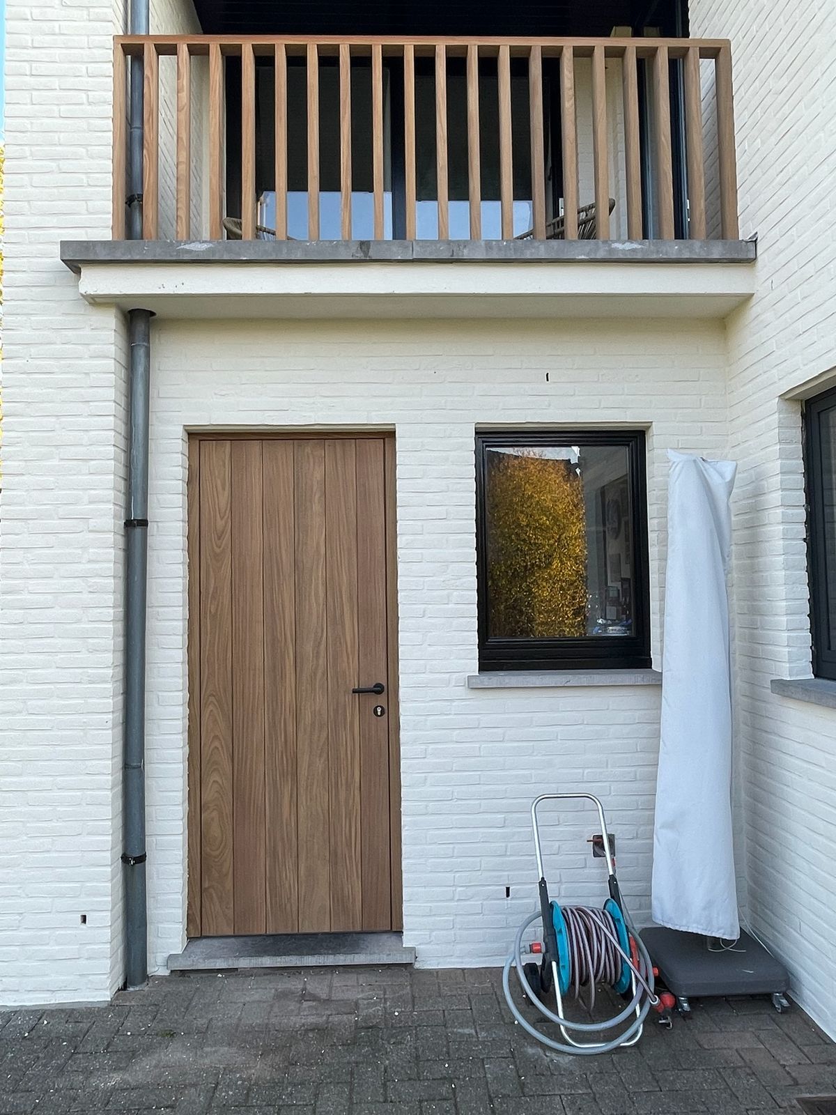 Houten buitendeur in witte gevel met houten balkonbalustrade erboven in Zevergem.