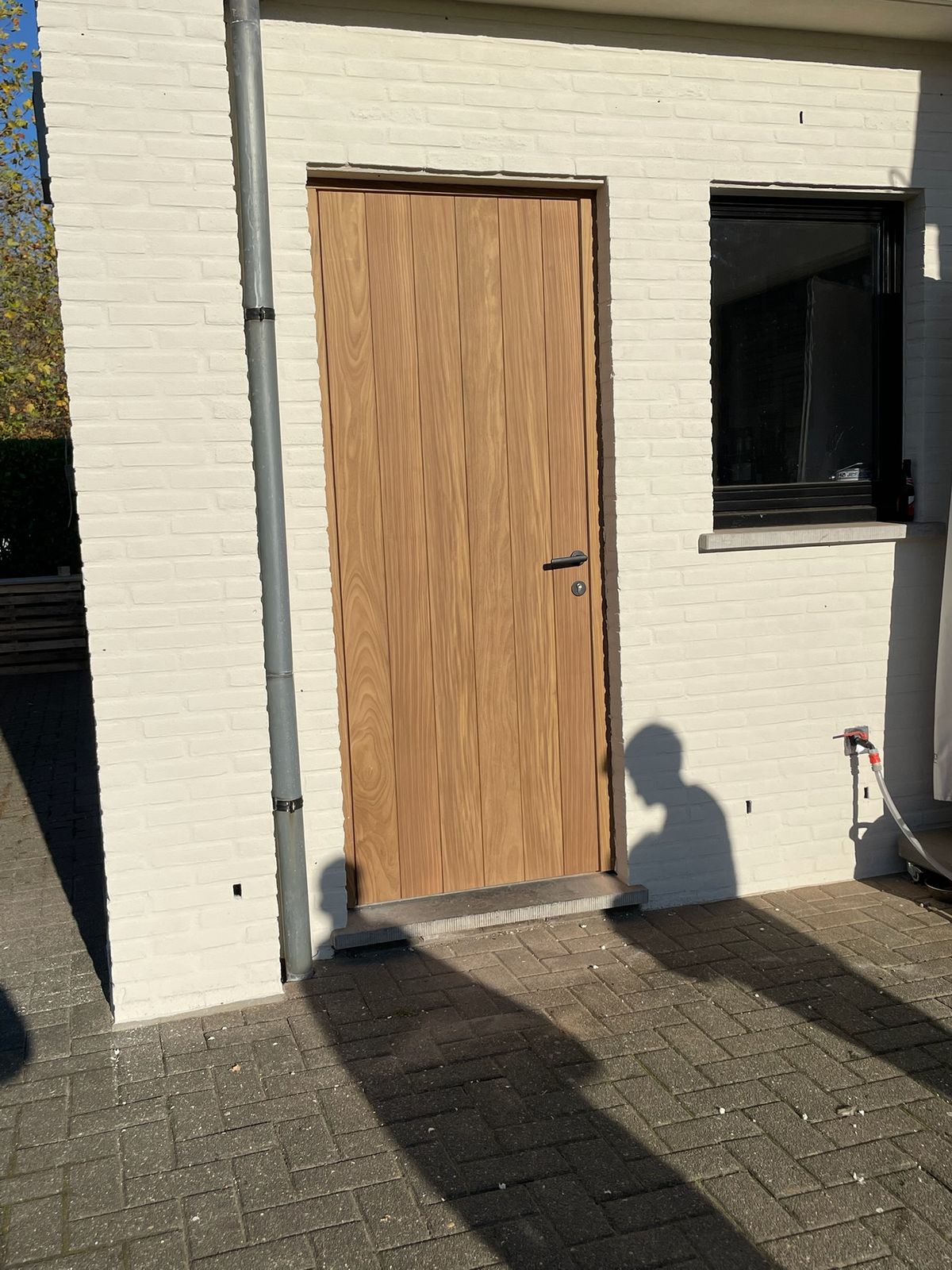 Nieuwe houten buitendeur in een witgeschilderde bakstenen gevel van een woning in Zevergem.