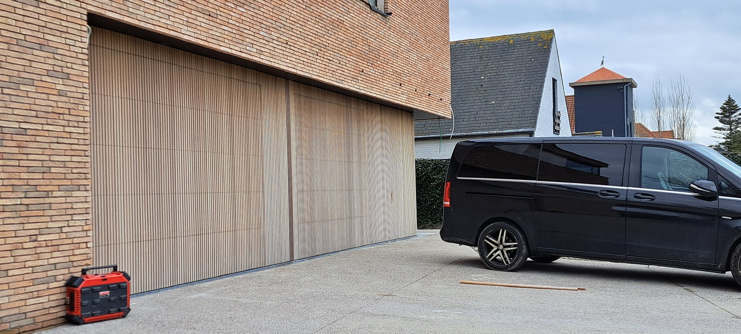 Houten garagepoort met verticale latten op maat in een bakstenen gevel
