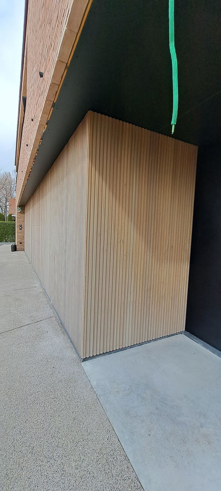 Houten garagepoort in verticale latten naadloos in de gevelbekleding in Knokke-Heist.