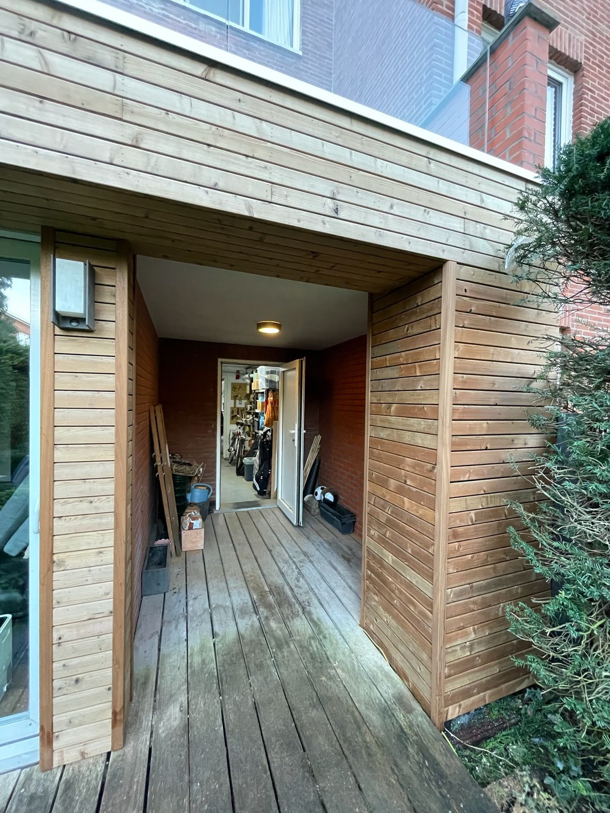 Houten gevelbekleding aan de tuinzijde rond een overdekte doorgang met houten vloer.