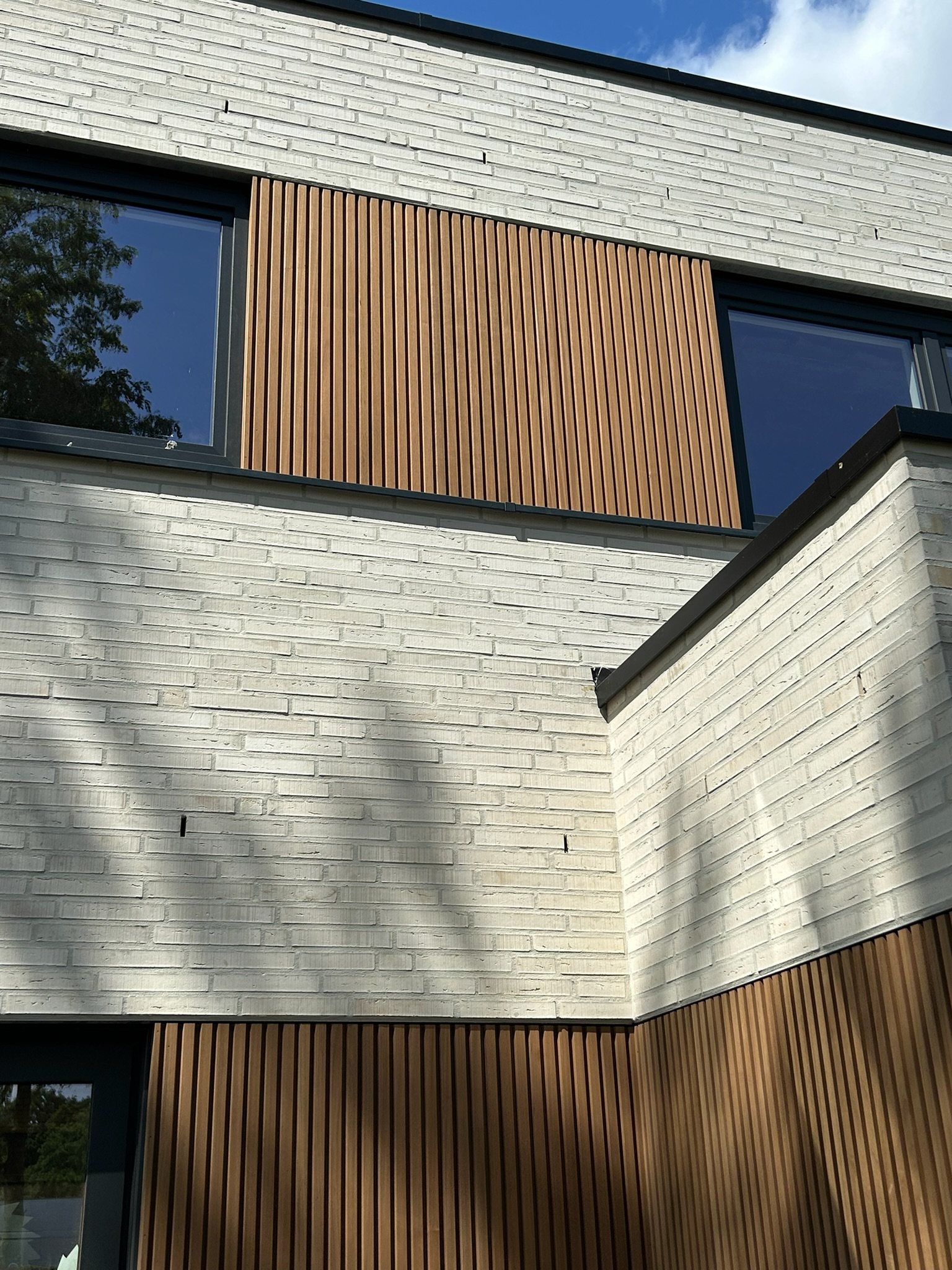 Verticale houten latten tussen witte baksteen en ramen in Beernem