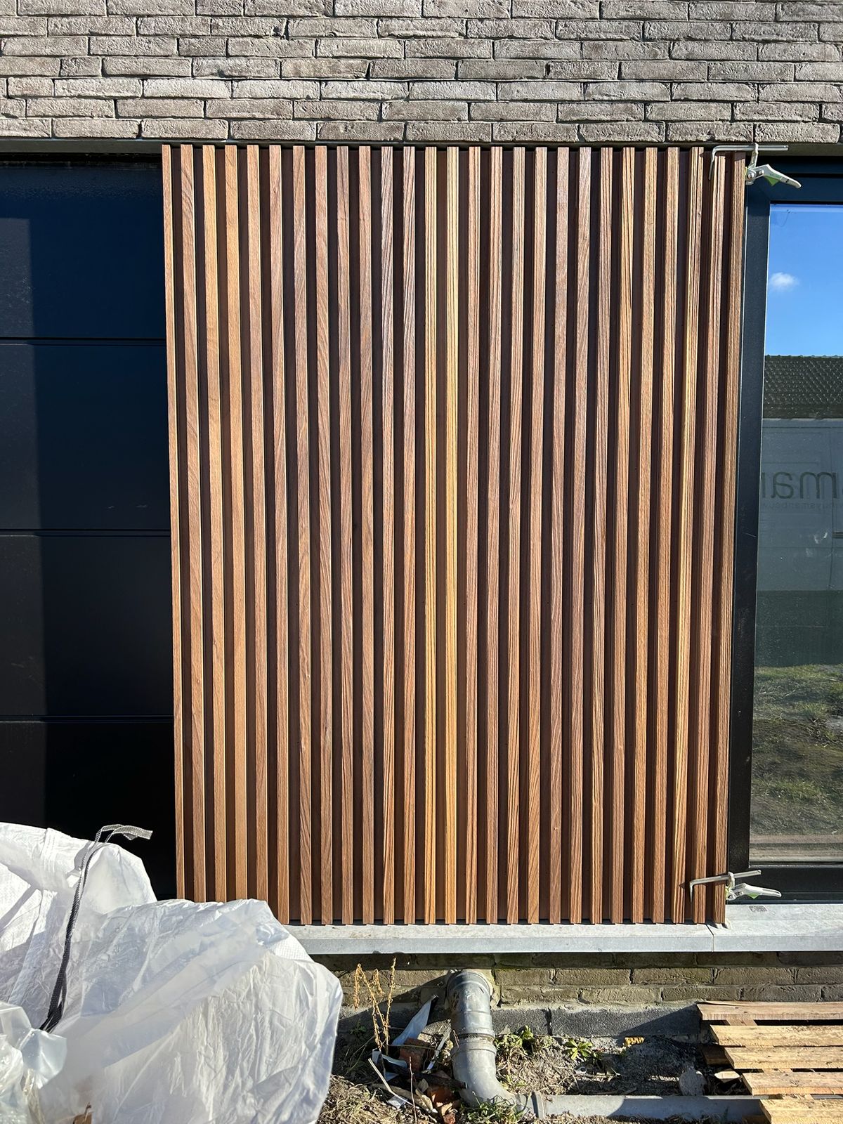 Detail van verticale houten latten als gevelbekleding tussen zwarte panelen in Bassevelde.