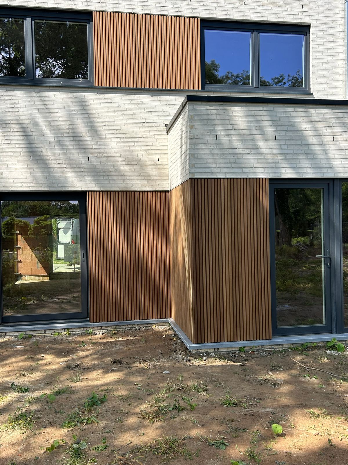 Nieuwbouw met witte steen en verticale houten gevelbekleding in latten rond de ramen in Beernem.