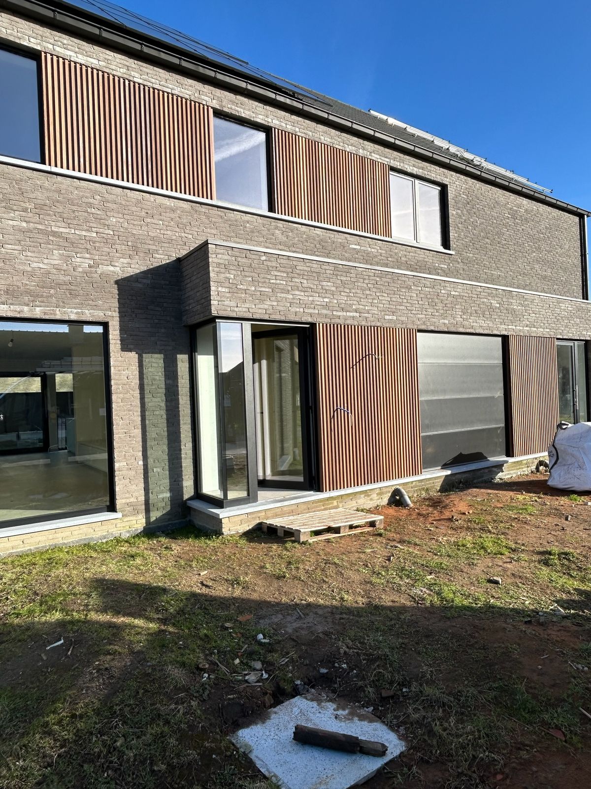 Woning in grijze baksteen met houten gevelbekleding in latten op beide verdiepingen in Bassevelde.
