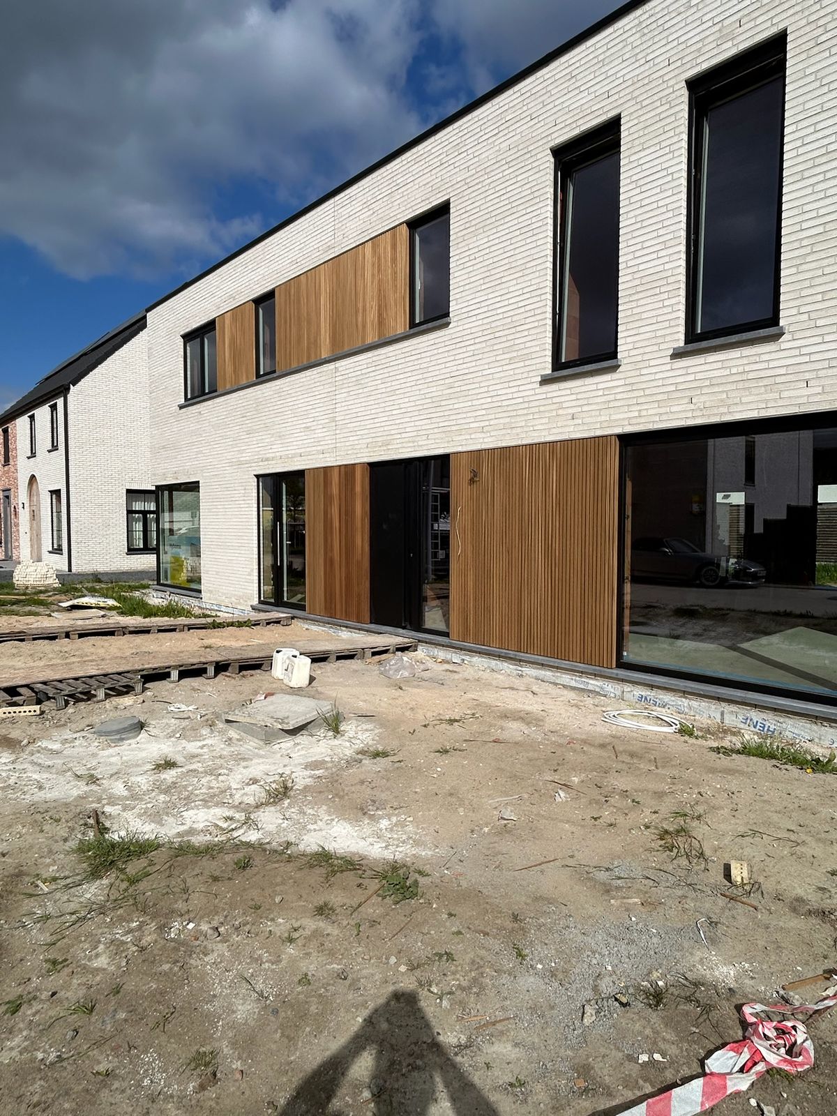 Nieuwbouwwoning in witte baksteen met houten gevelbekleding onder blauwe lucht in Ardooie.