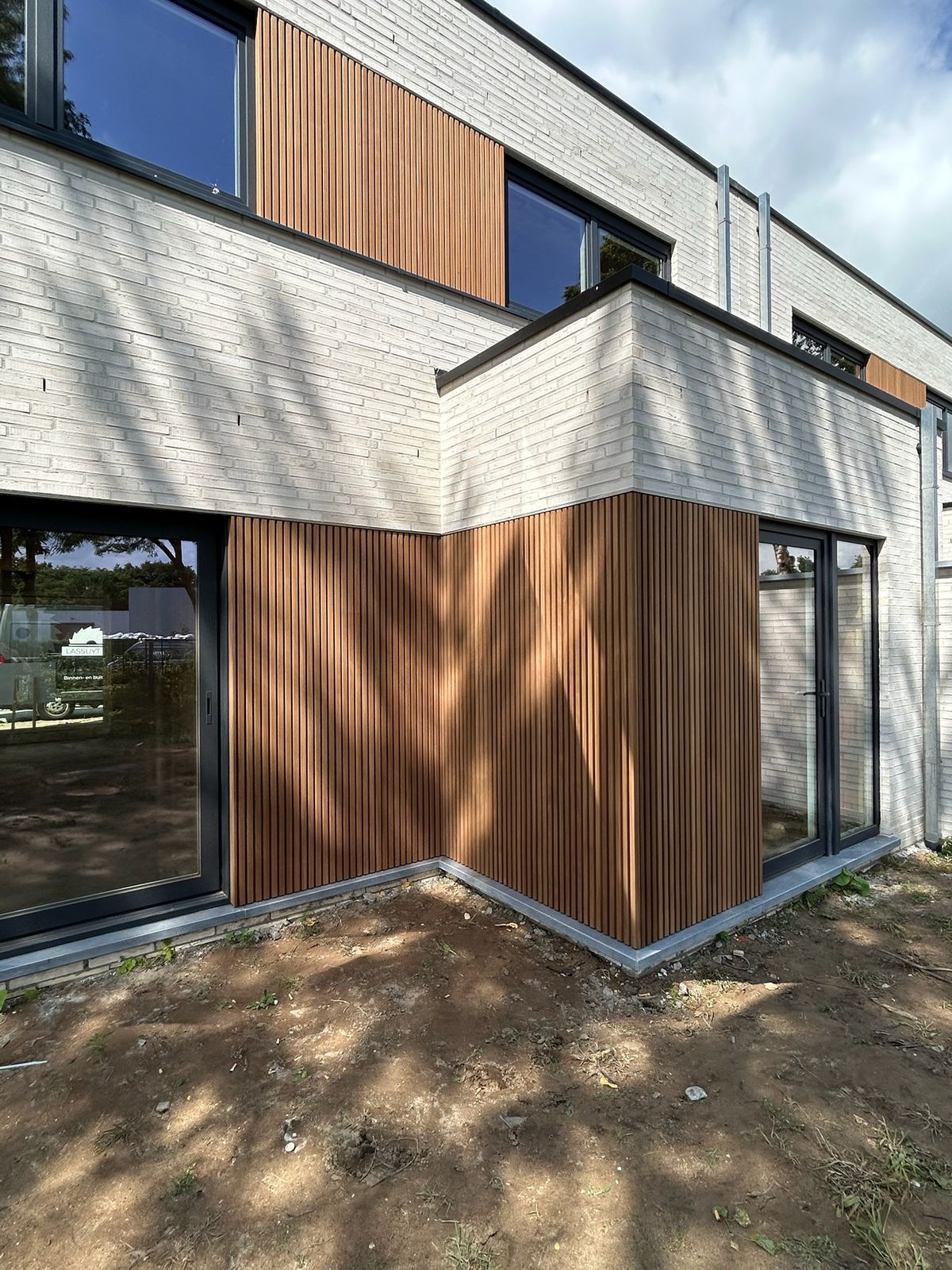 Houten latten gevelbekleding rond de hoek van een witte nieuwbouwwoning in Beernem.