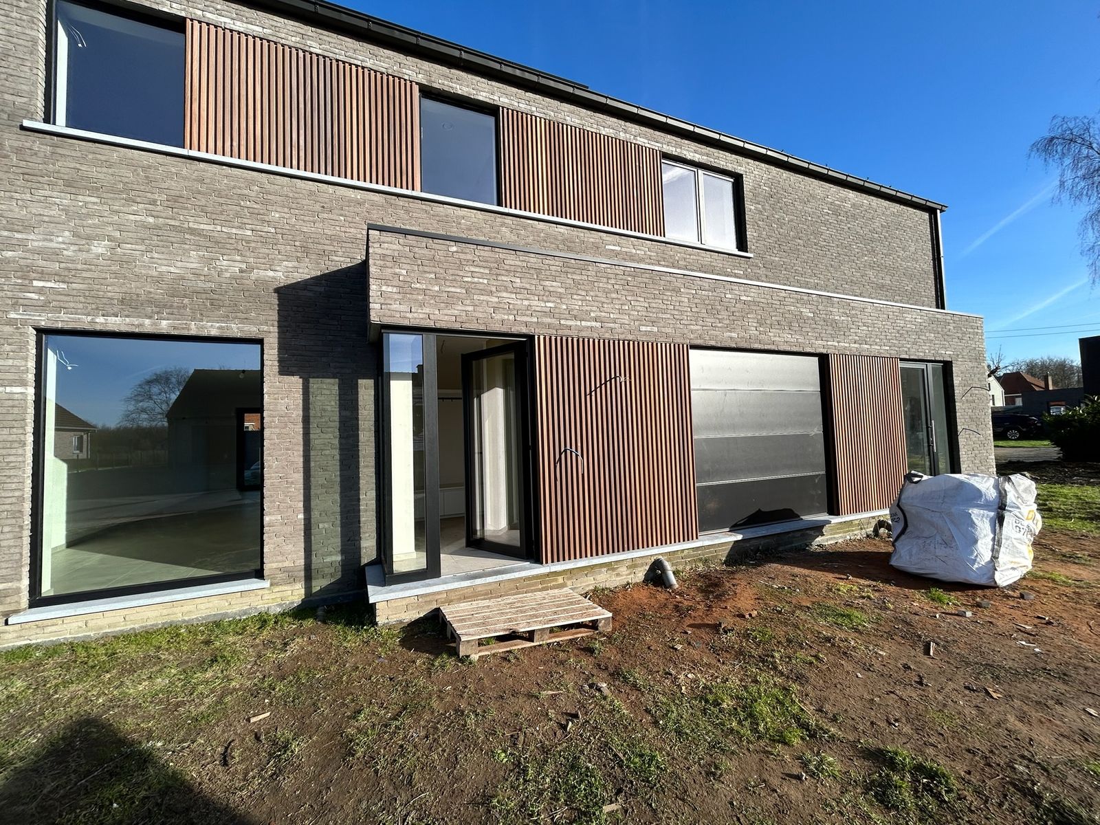 Nieuwbouw met houten latten als gevelbekleding naast grote ramen in Bassevelde.