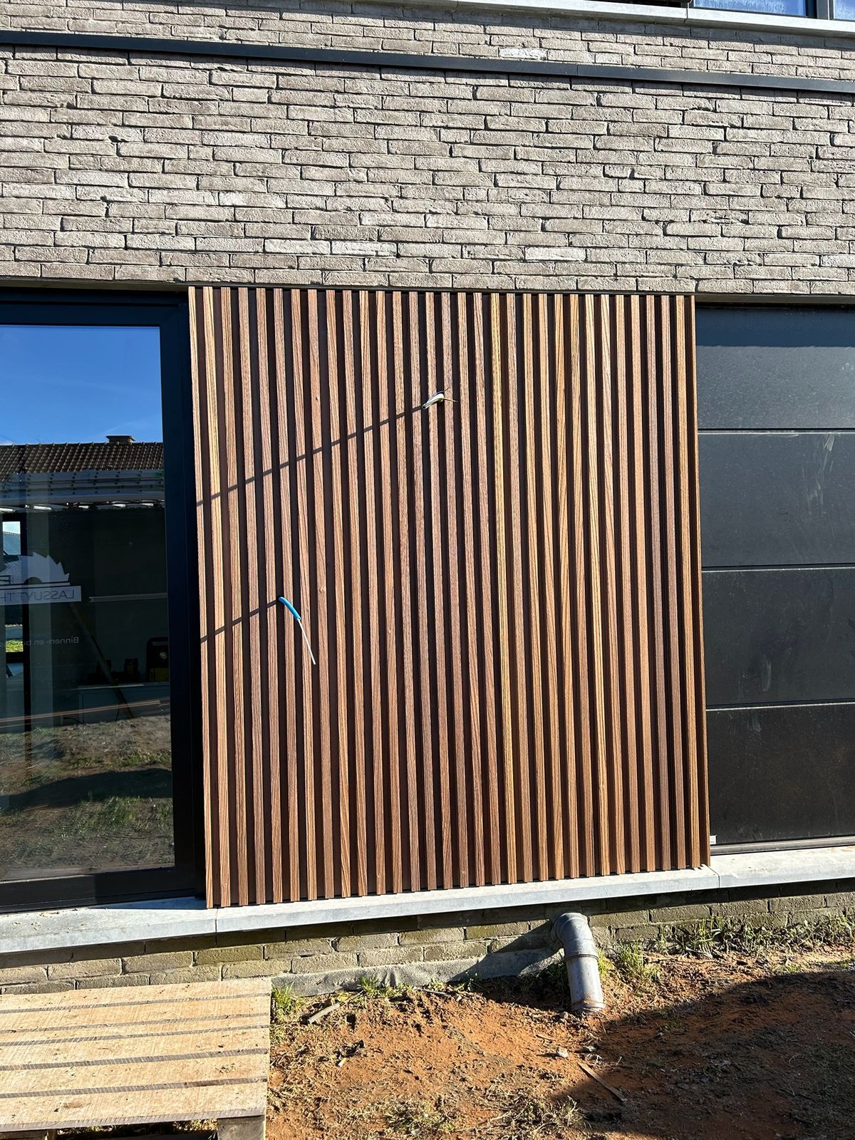Houten gevelbekleding in latten tussen een raam en zwarte panelen in Bassevelde.