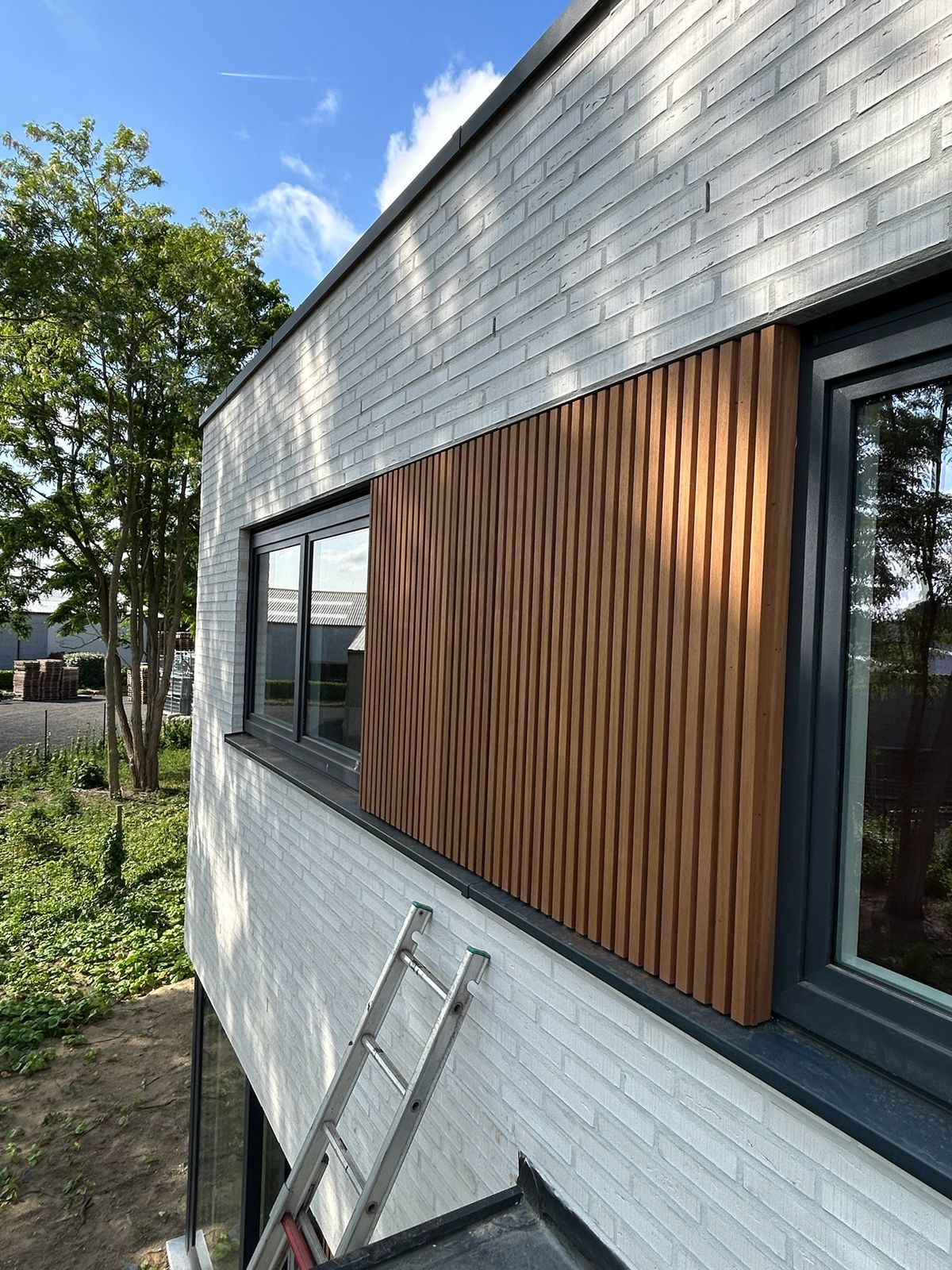 Verticale houten latten als gevelbekleding tussen twee ramen op de verdieping in Beernem.