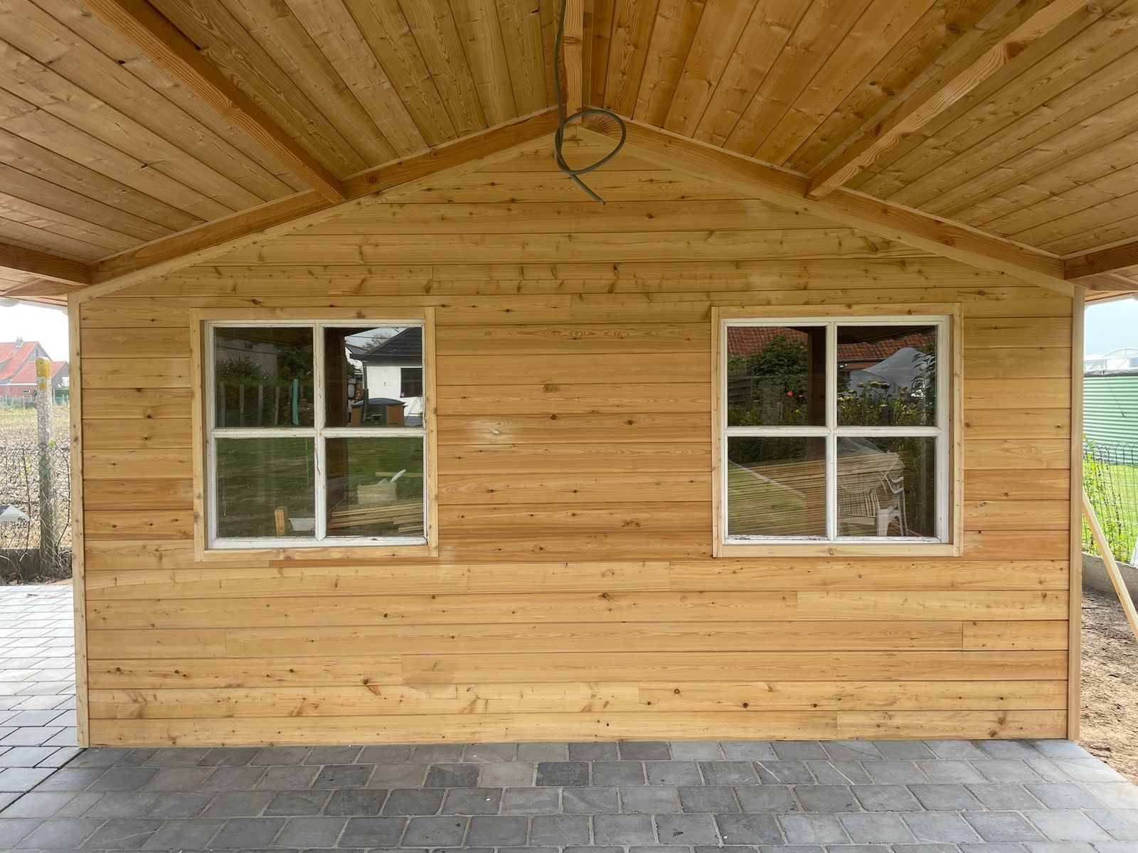 Gevel van een houten poolhouse met twee ramen onder een houten plafond in Machelen.