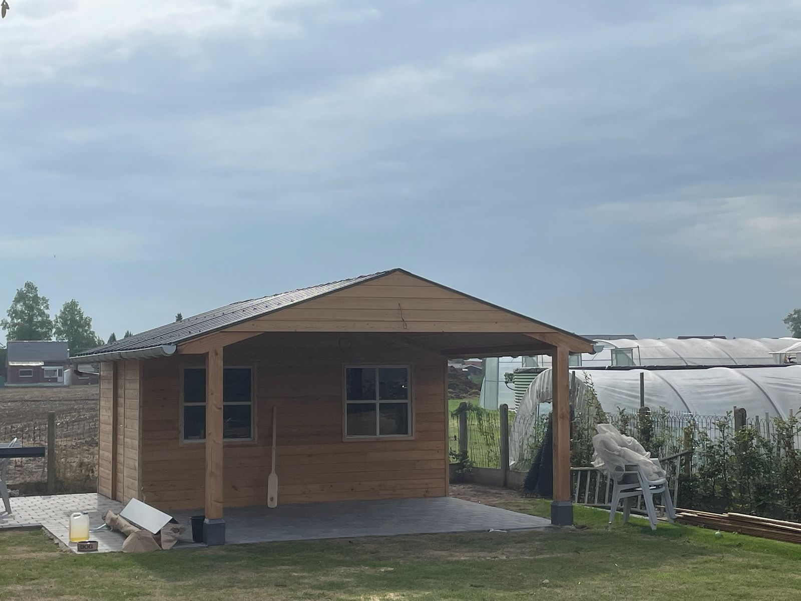 Houten poolhouse met zadeldak en open overkapping op een grasveld in Machelen.