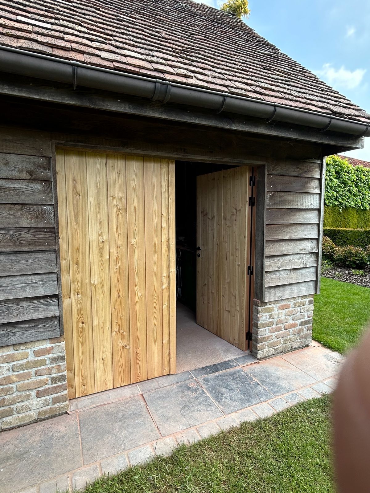 Nieuwe houten schuurpoorten in een bijgebouw met houten gevel in Poesele.