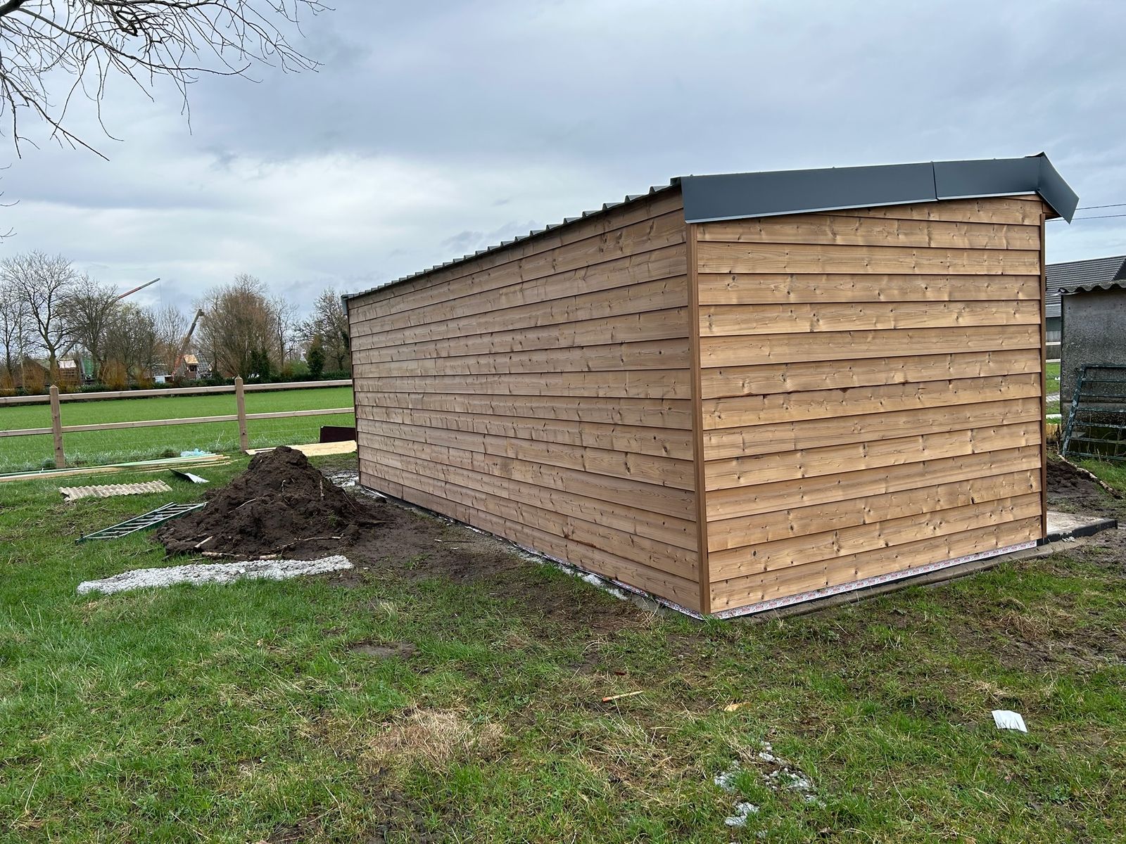 Houten stal met horizontale planken en plat dak in een weide in Lotenhulle.