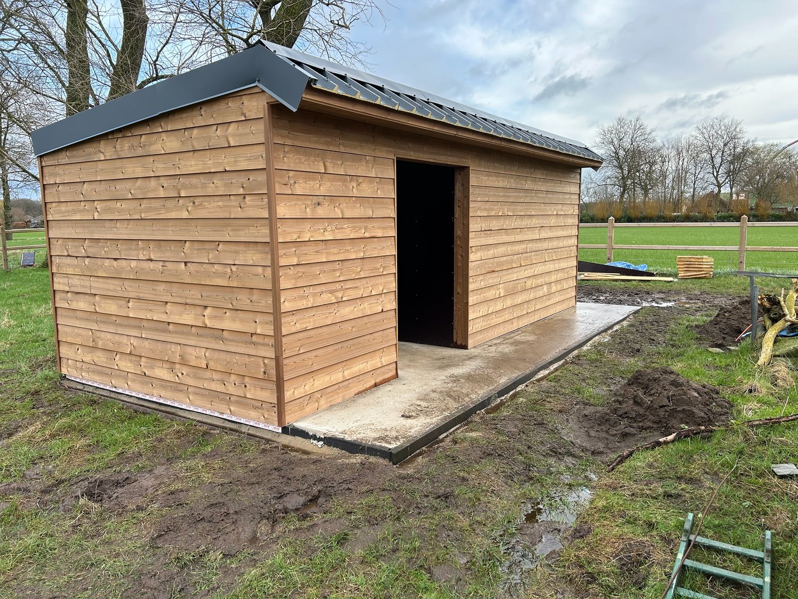 Nieuw gebouwde houten stal met open deuropening op een weide in Lotenhulle.