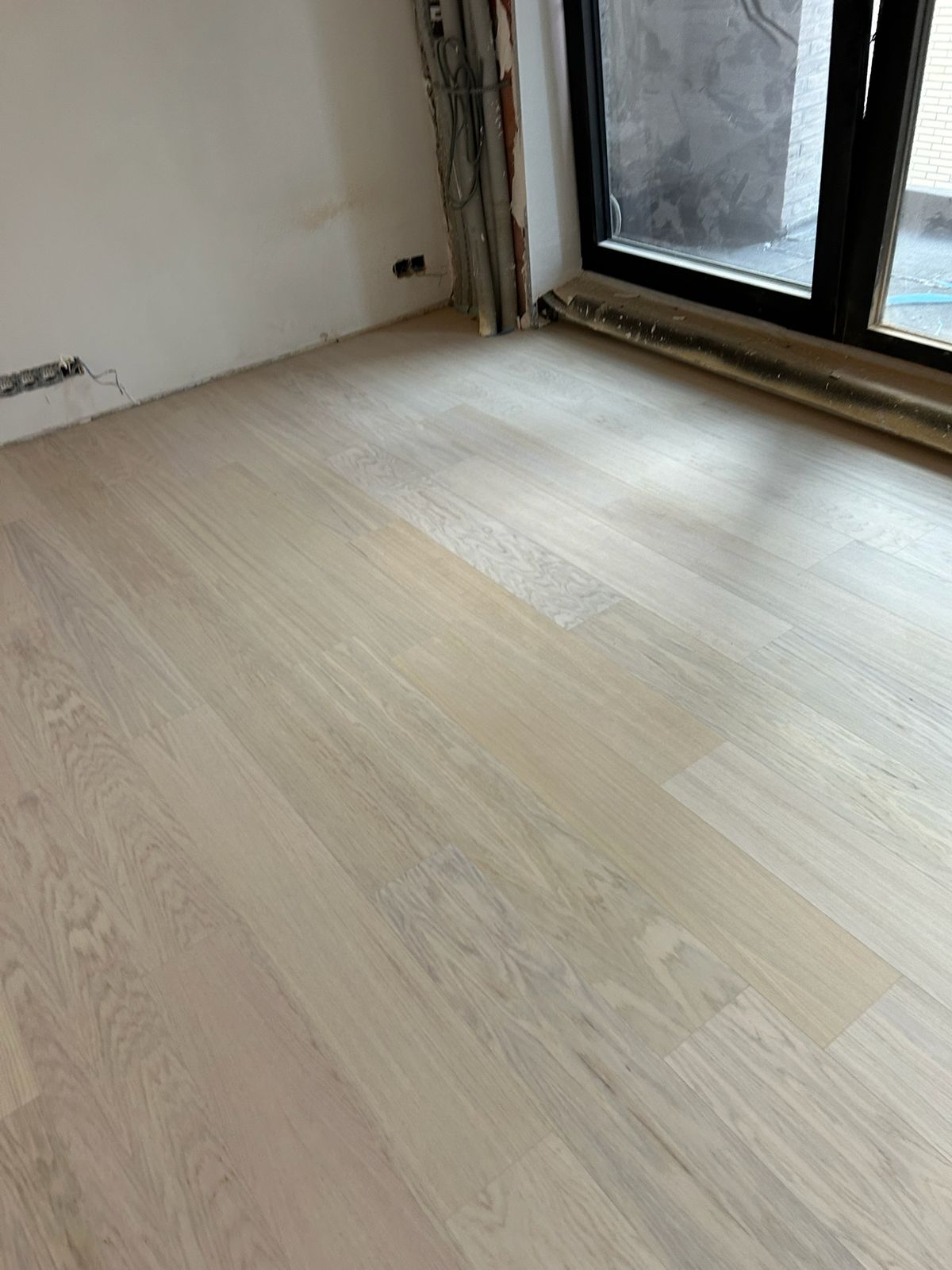 Lichte houten parketvloer gelegd in een kamer met groot raam in Kortrijk.