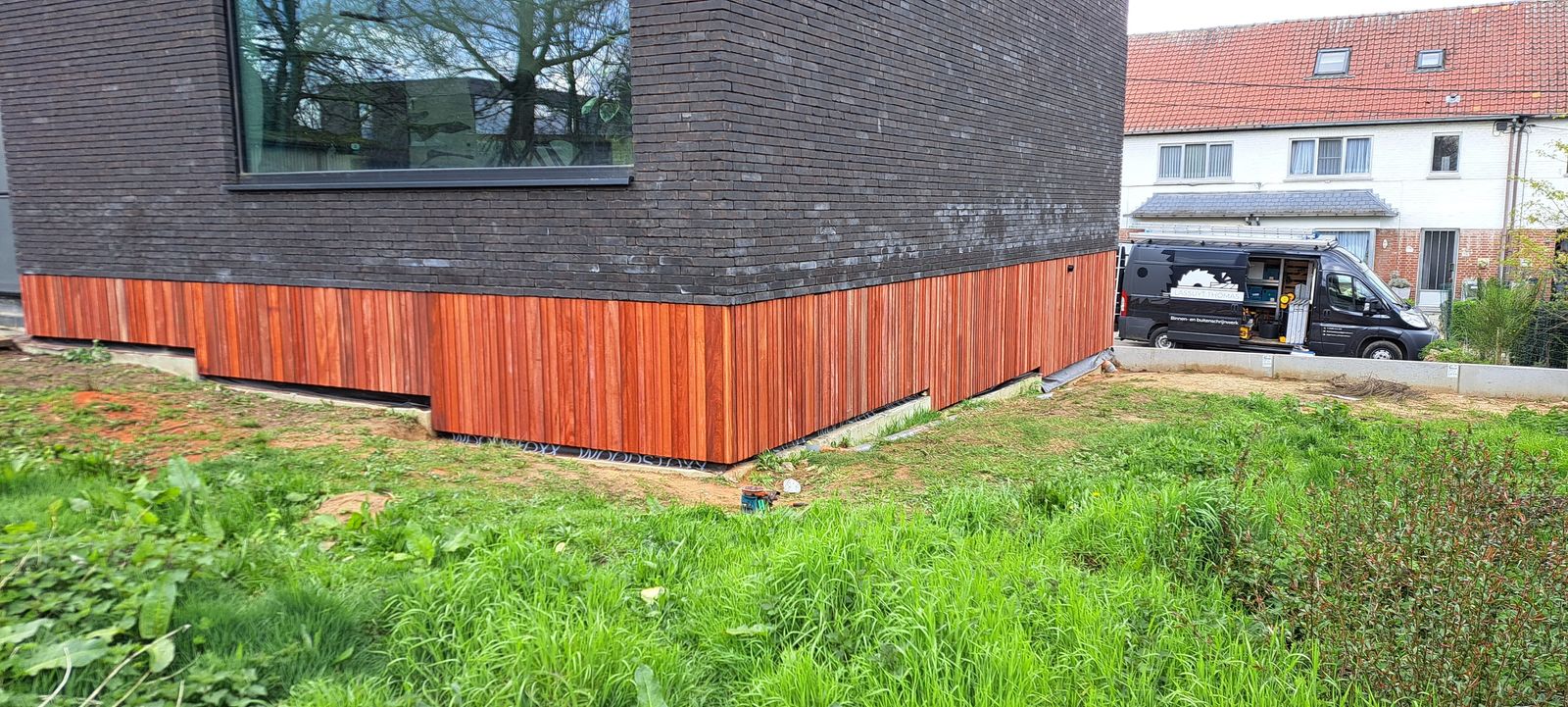 Gelijkvloers bekleed met padoek planken onder een donkere gevel met grasveld ervoor in Wintam.