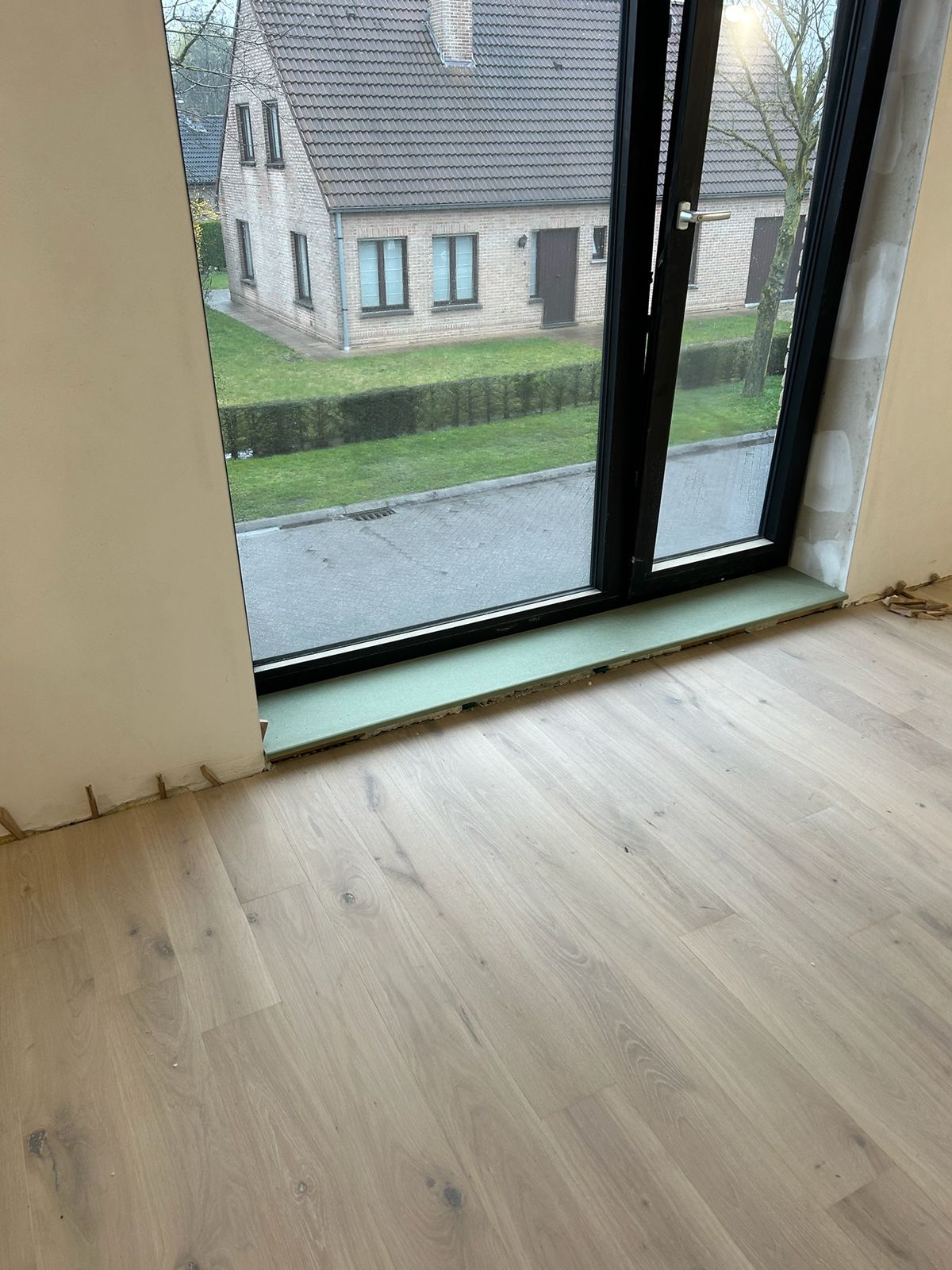 Raamtablet onder een groot zwart raam met lichte houten vloer in een woning in De Pinte.