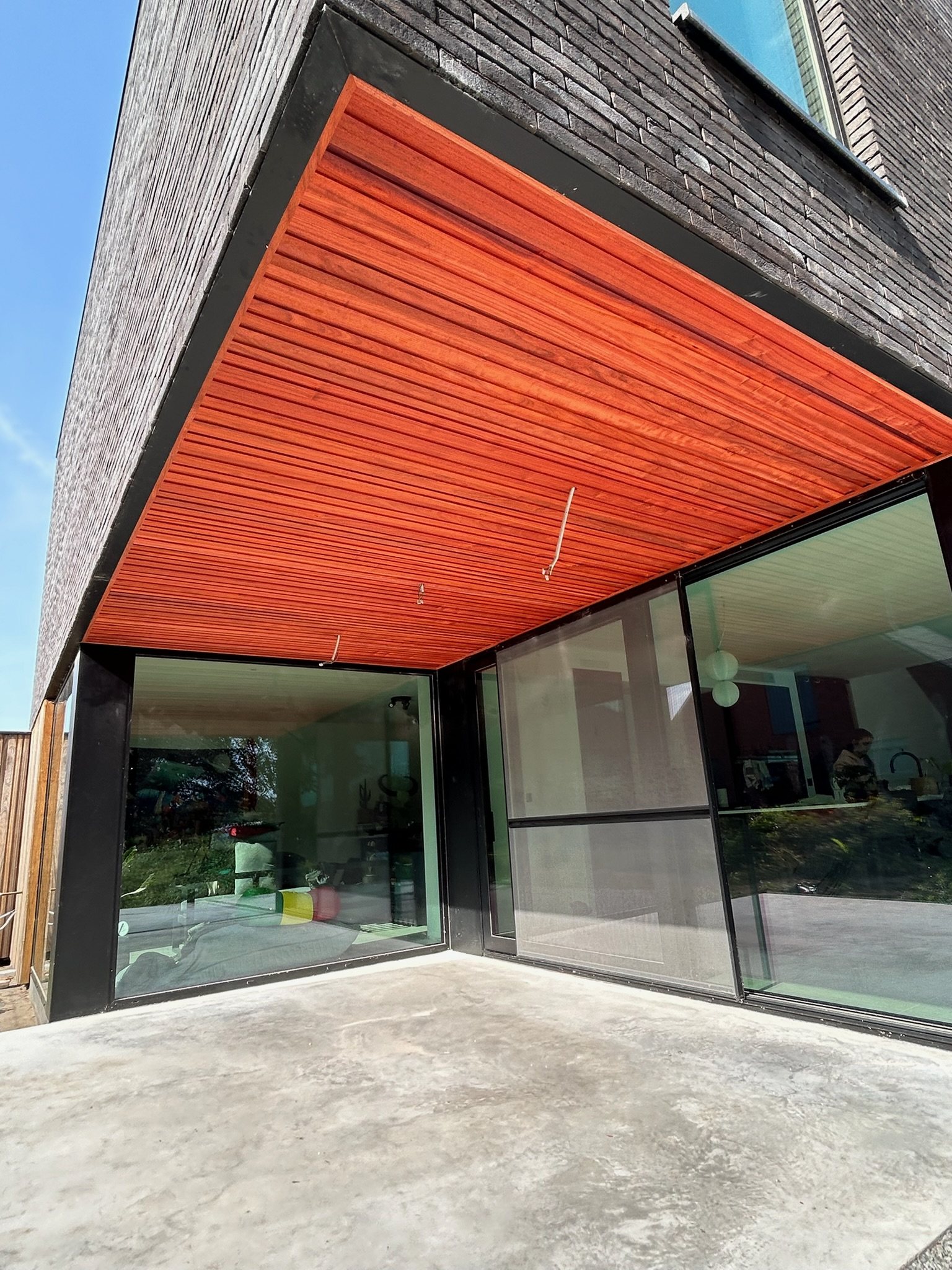 Houten plafond in rood hout boven een glazen hoek van een woning in Wintam