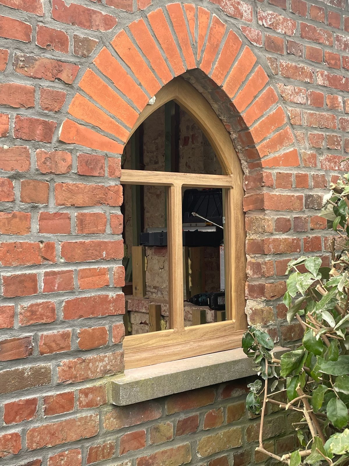 Houten spitsboograam op maat in een oude bakstenen gevel met gemetselde boog in Waregem.