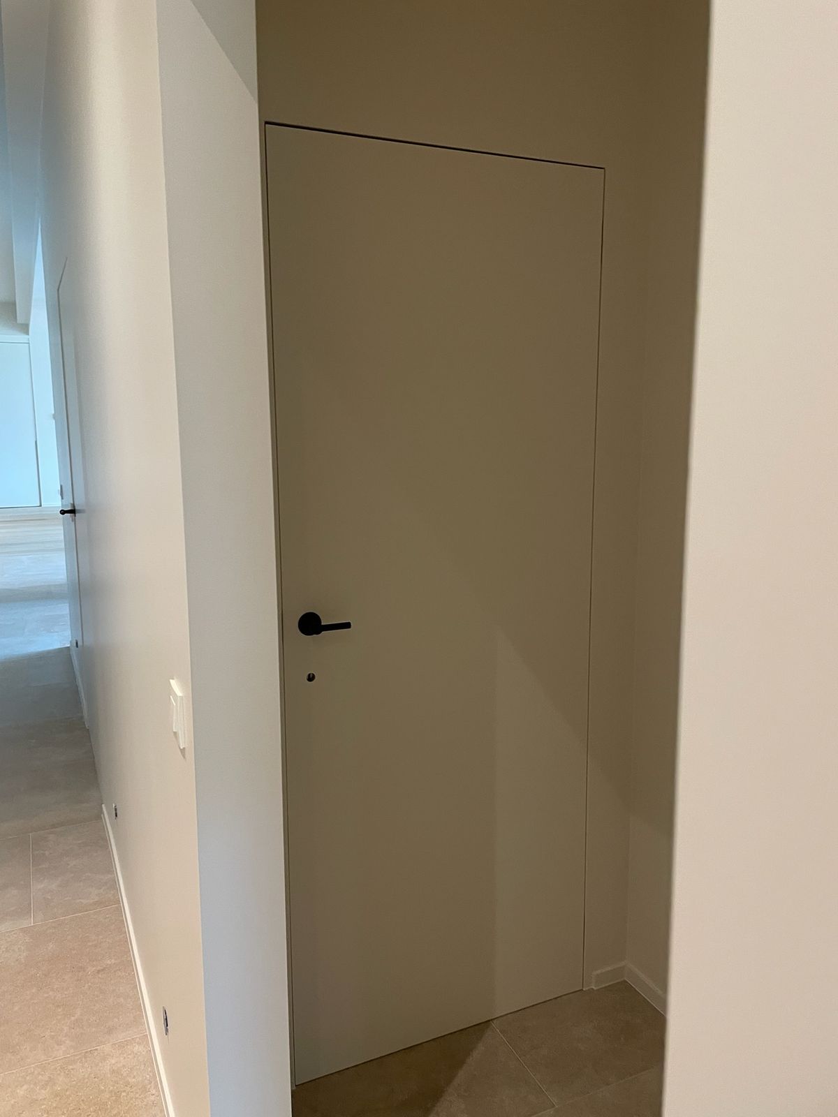 Verdoken binnendeur vlak in de wand met zwarte klink in een lichte gang in Meulebeke.