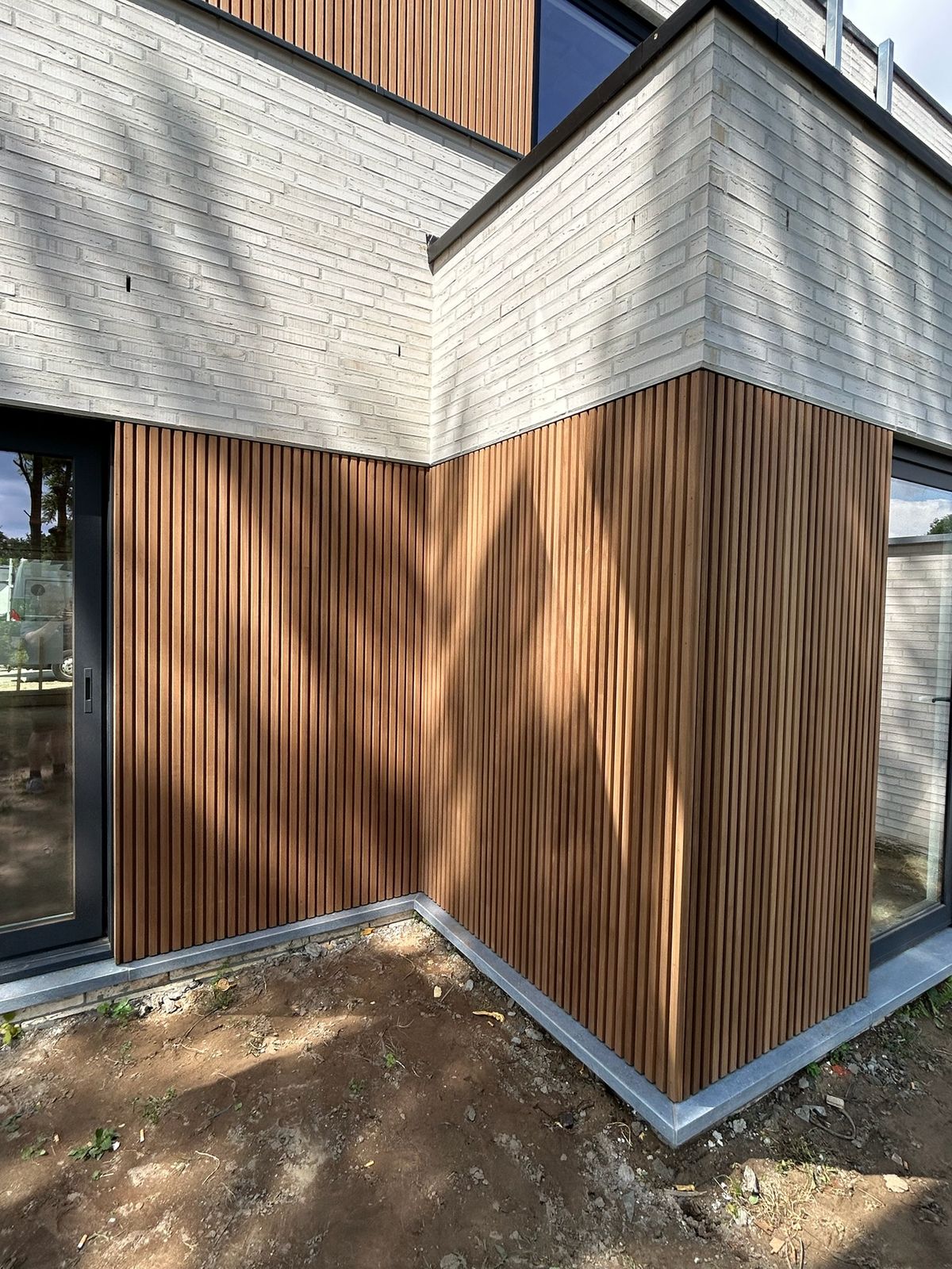 Detail van verticale houten latten op een binnenhoek onder witte gevelsteen in Beernem.